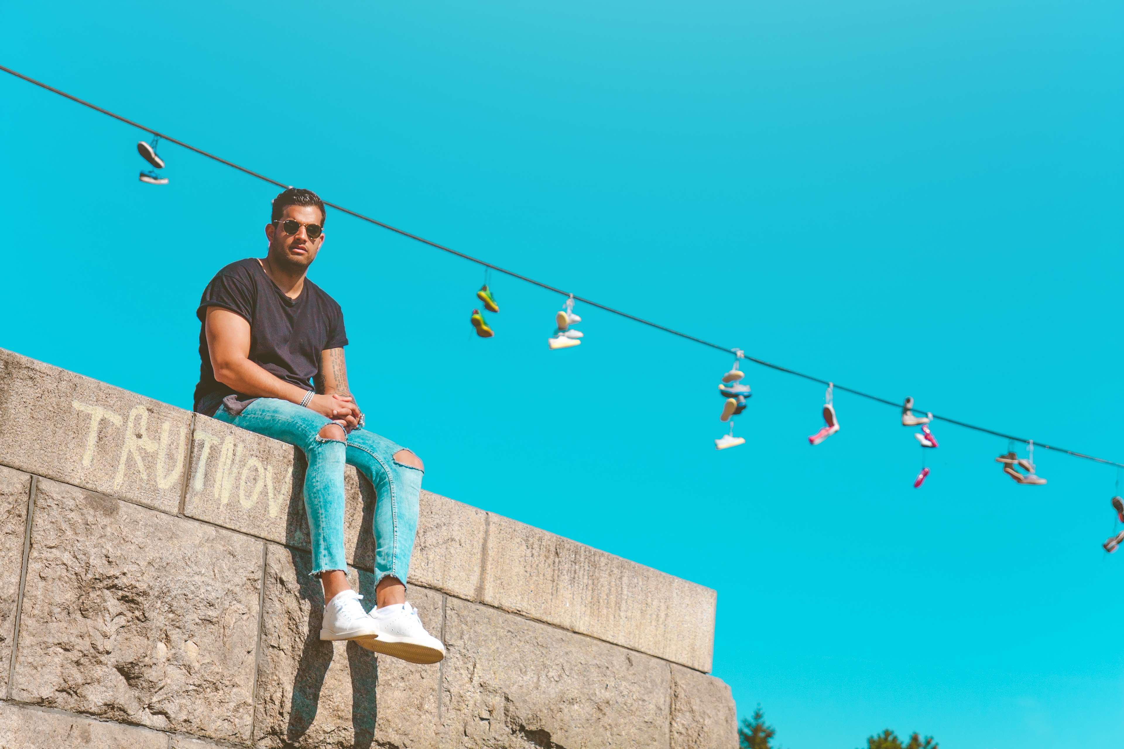 Man sitting on wall with shoes hanging on wire HD Wallpaper