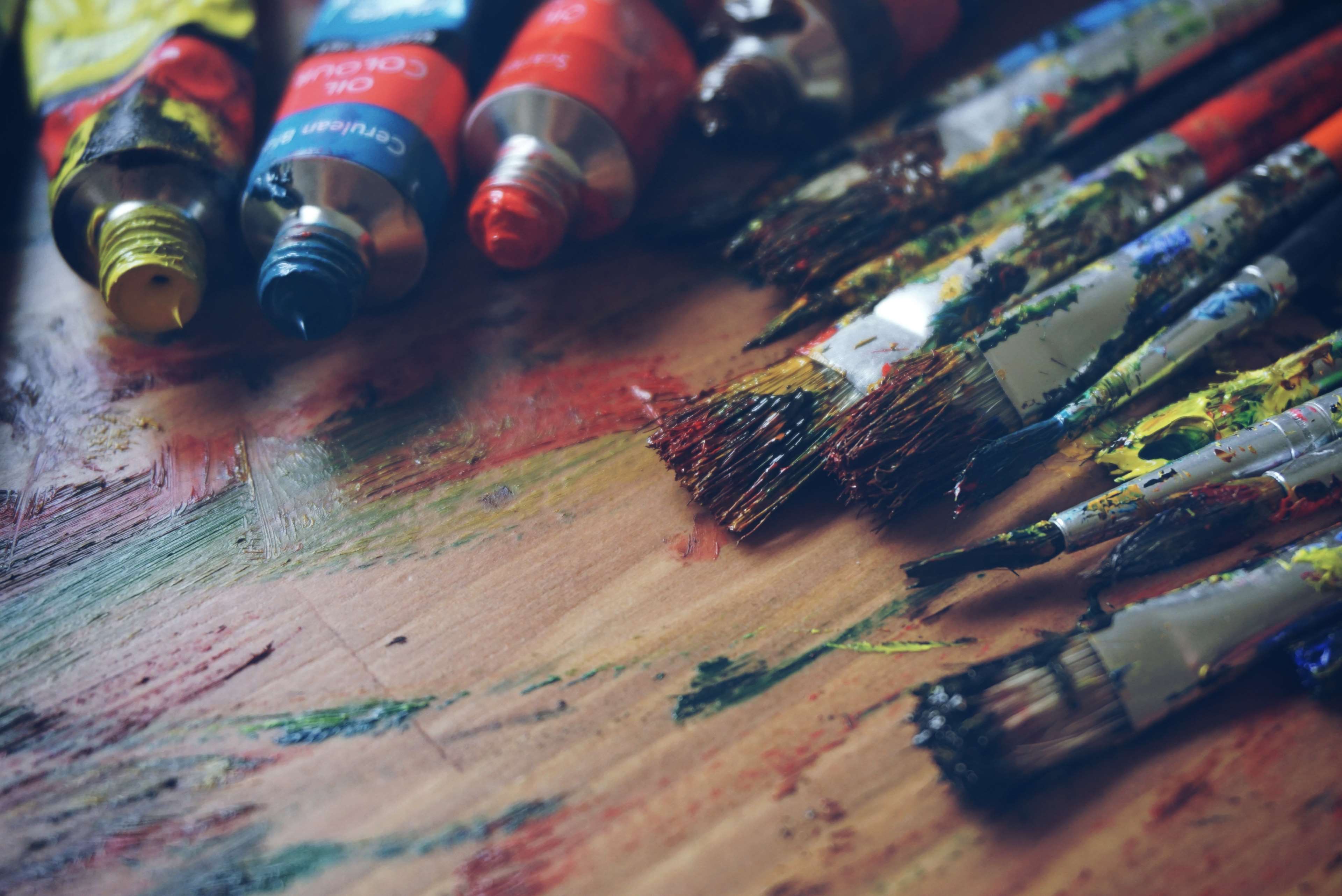 Paint tubes and brushes on a colorful wooden surface HD Wallpaper