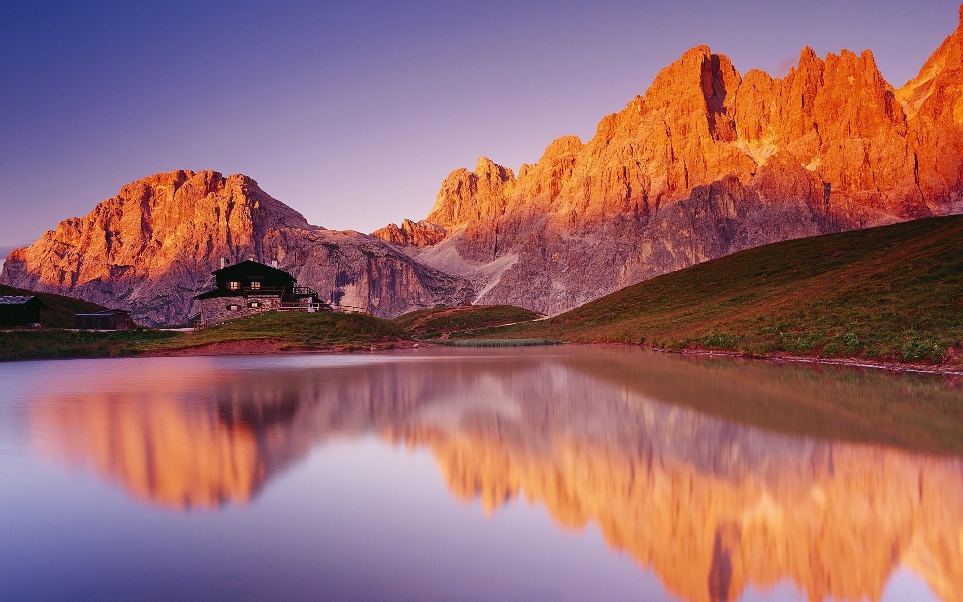 Mountain lodge reflected in a calm lake at sunrise HD Wallpaper