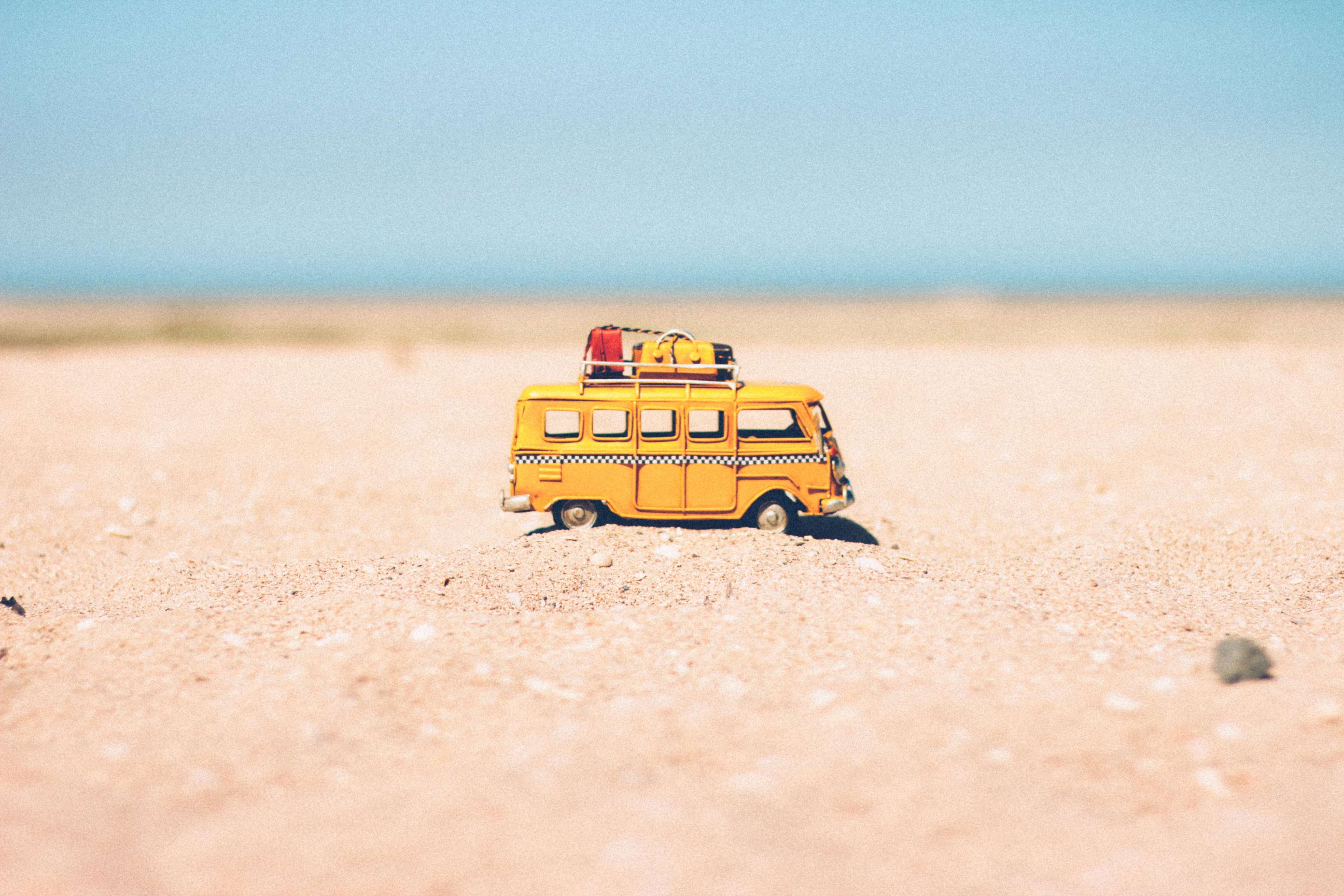 Yellow toy van with luggage on sand HD Wallpaper