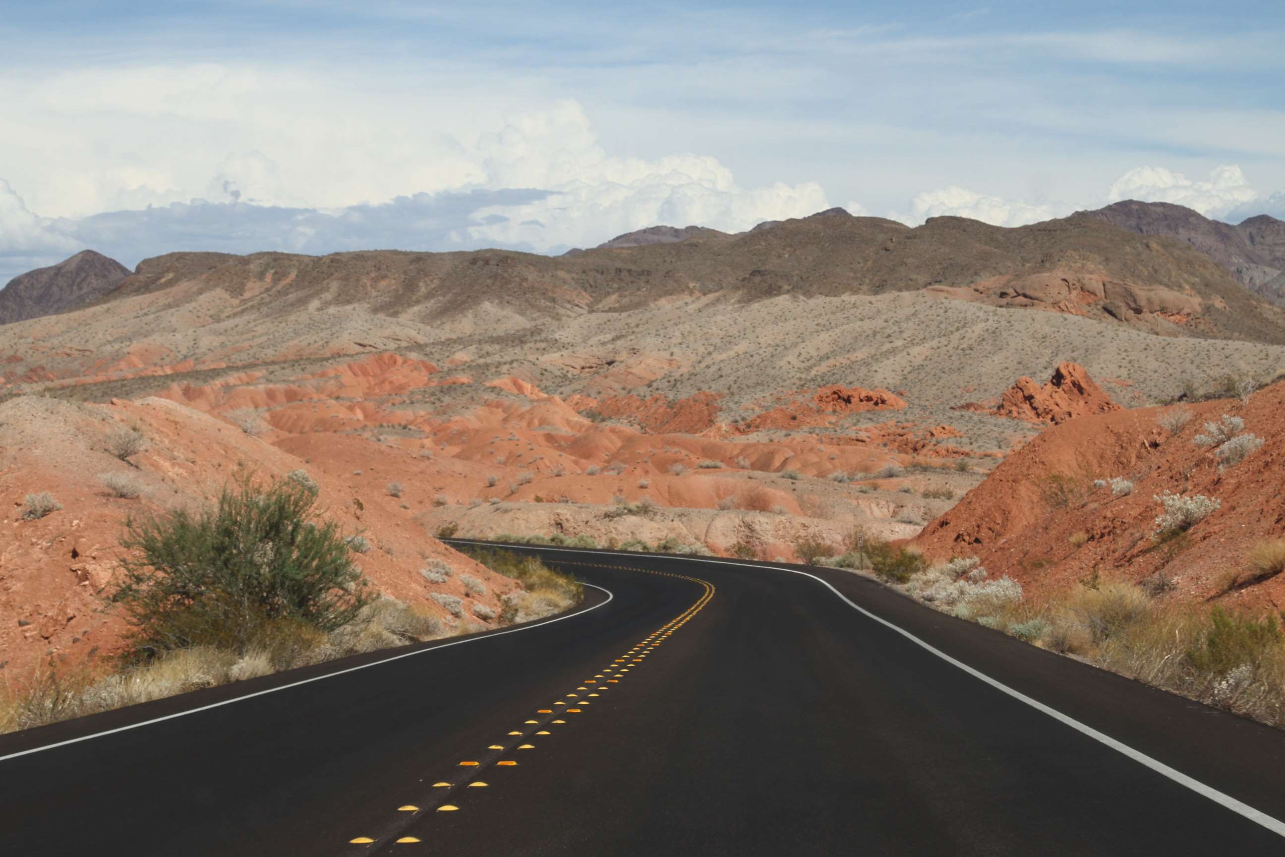 Desert highway winding through red rock mountains under a cloudy sky HD Wallpaper