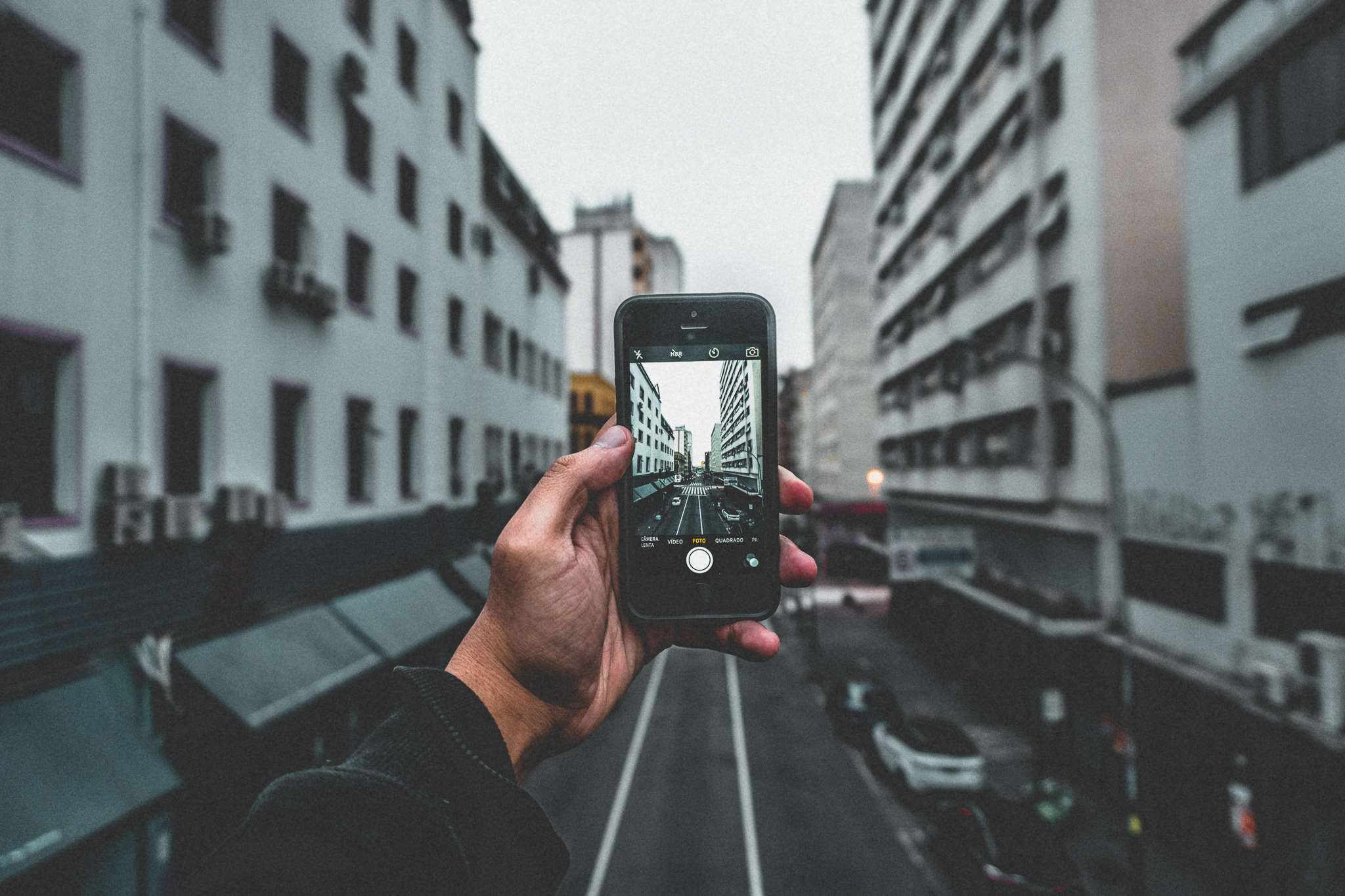 Hand holding iPhone taking picture of city street HD Wallpaper