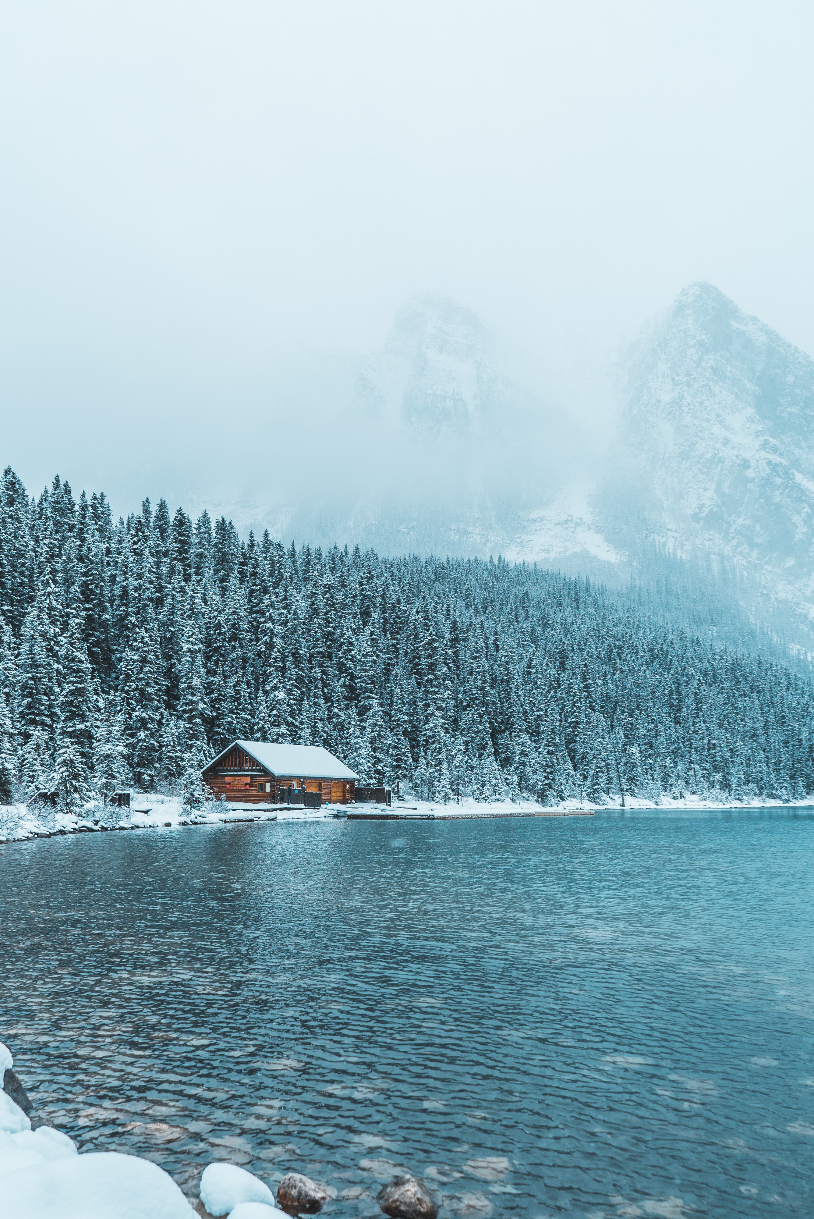 Log cabin by a lake with snow-covered trees and mountains HD Wallpaper