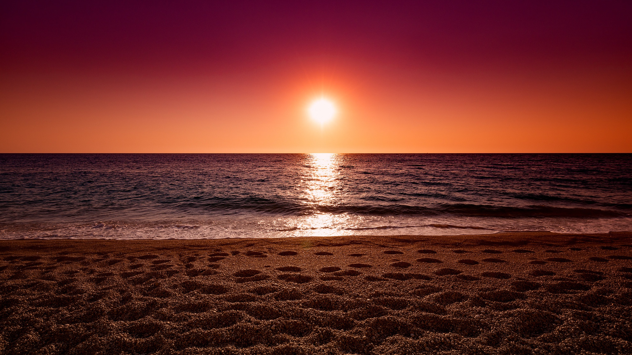 Sunset over the ocean with footprints on the sand HD Wallpaper