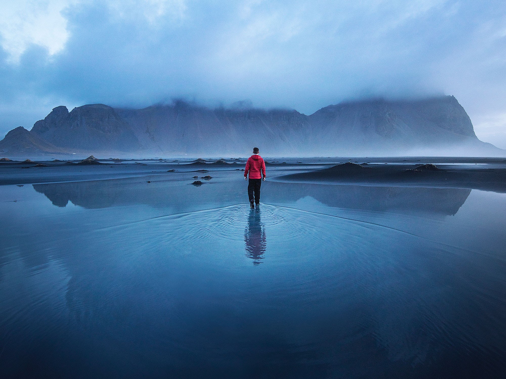 Man walking on a wet beach with mountains in the background HD Wallpaper