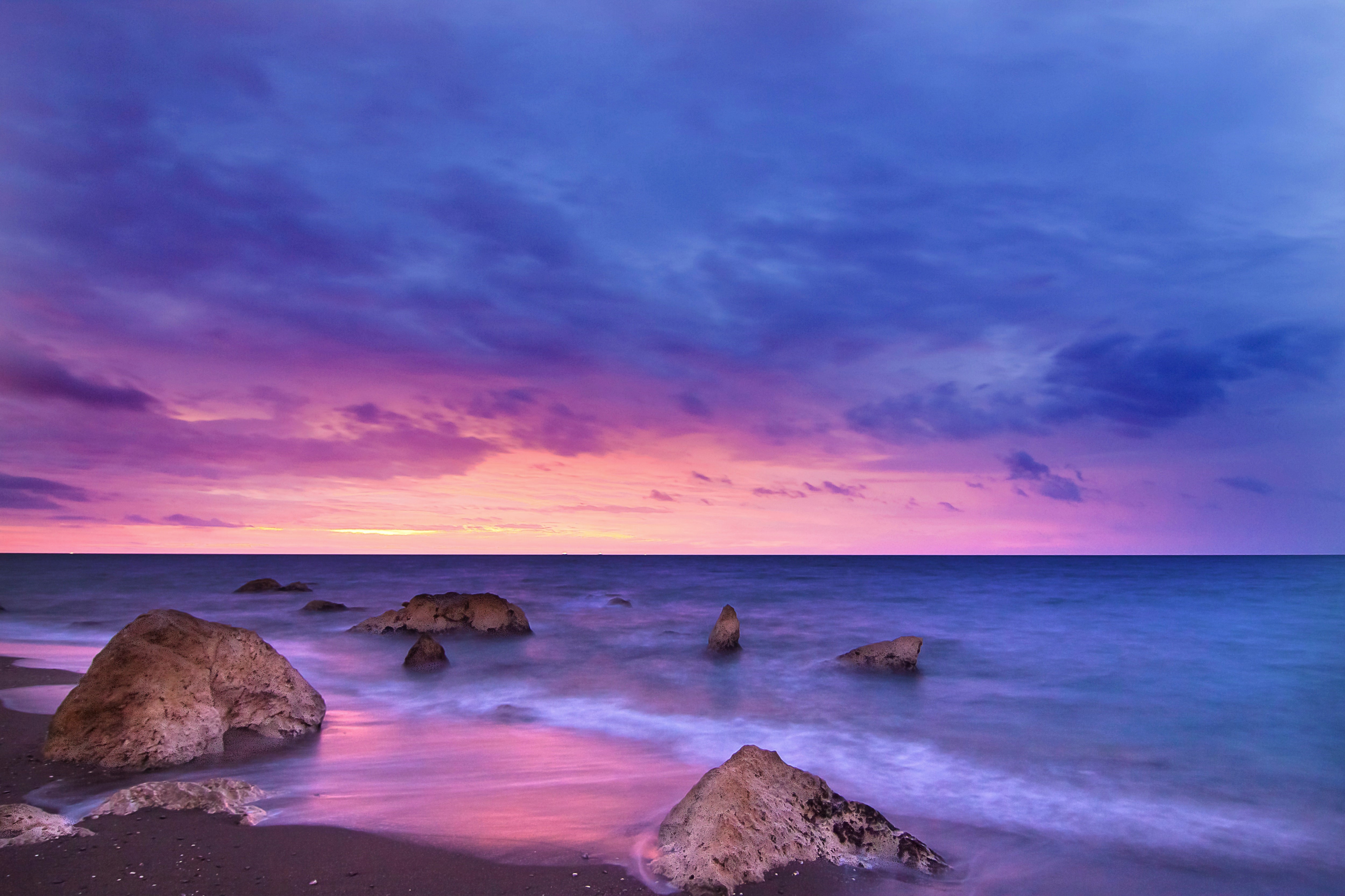 Sunset over a rocky beach with purple and pink clouds HD Wallpaper