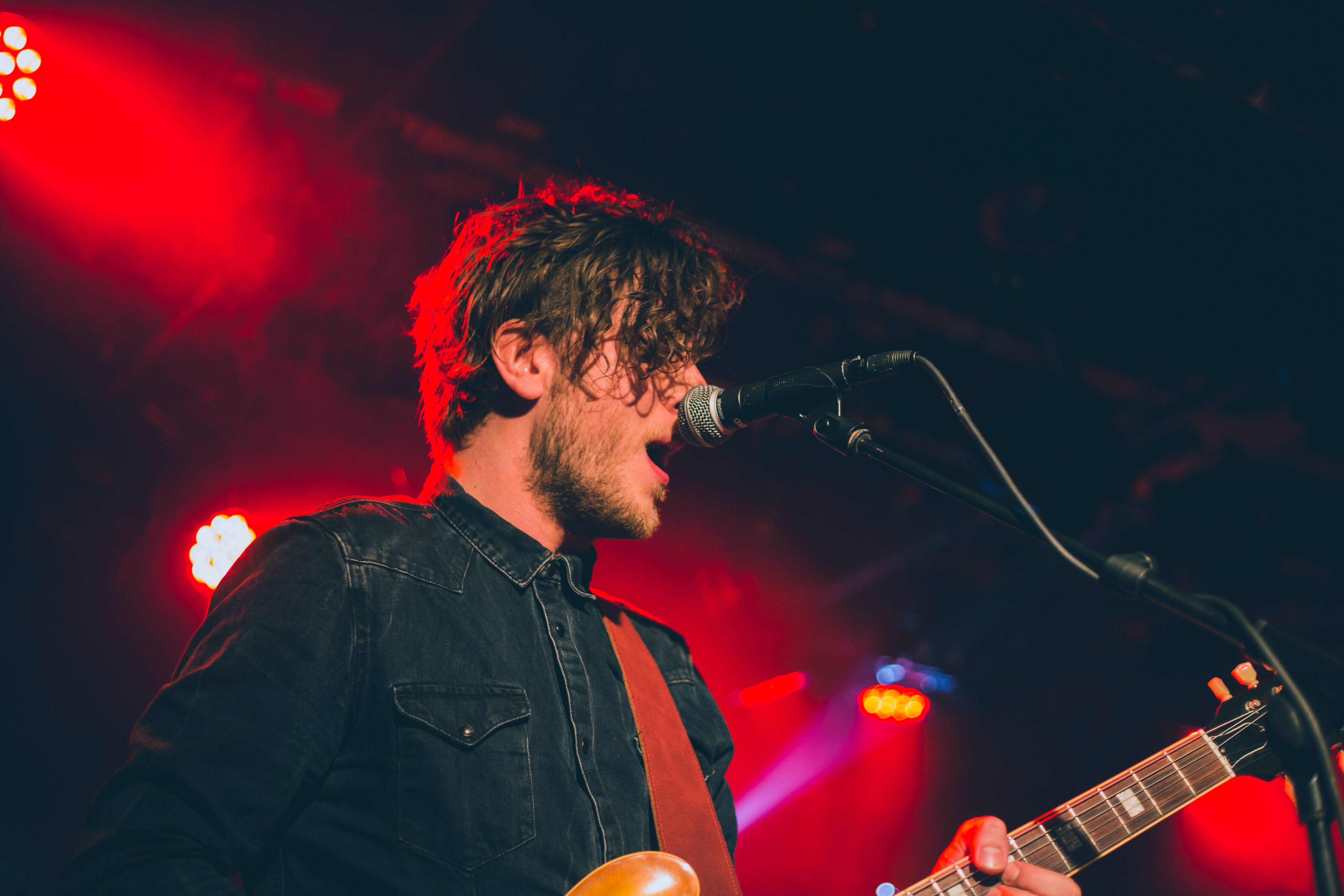 Male guitarist singing into microphone on stage HD Wallpaper