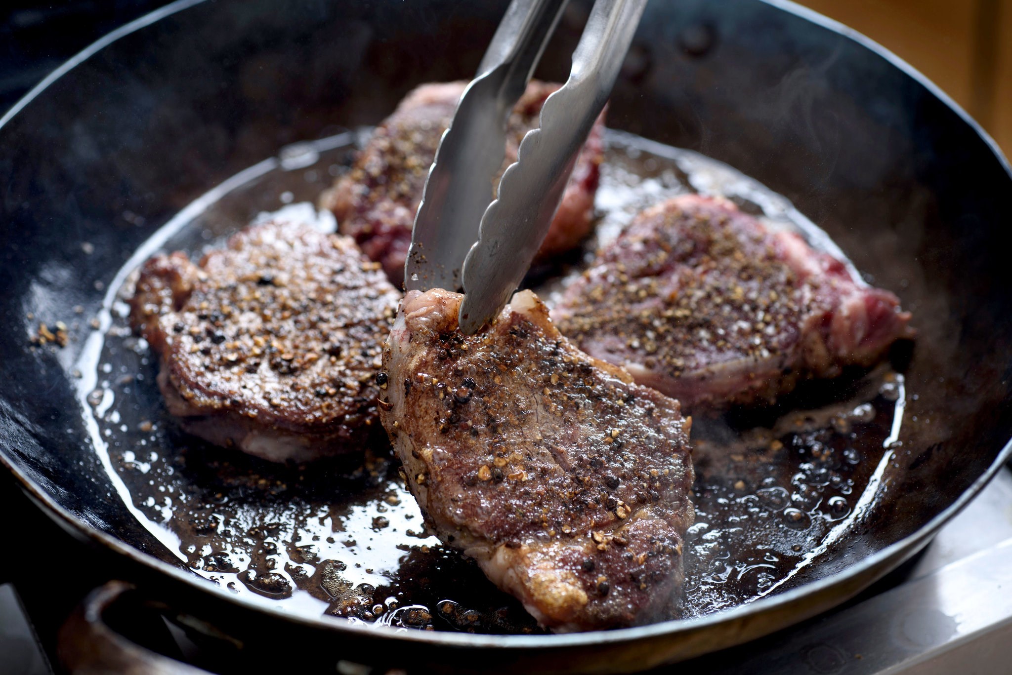 Steaks being seared in a cast iron pan HD Wallpaper