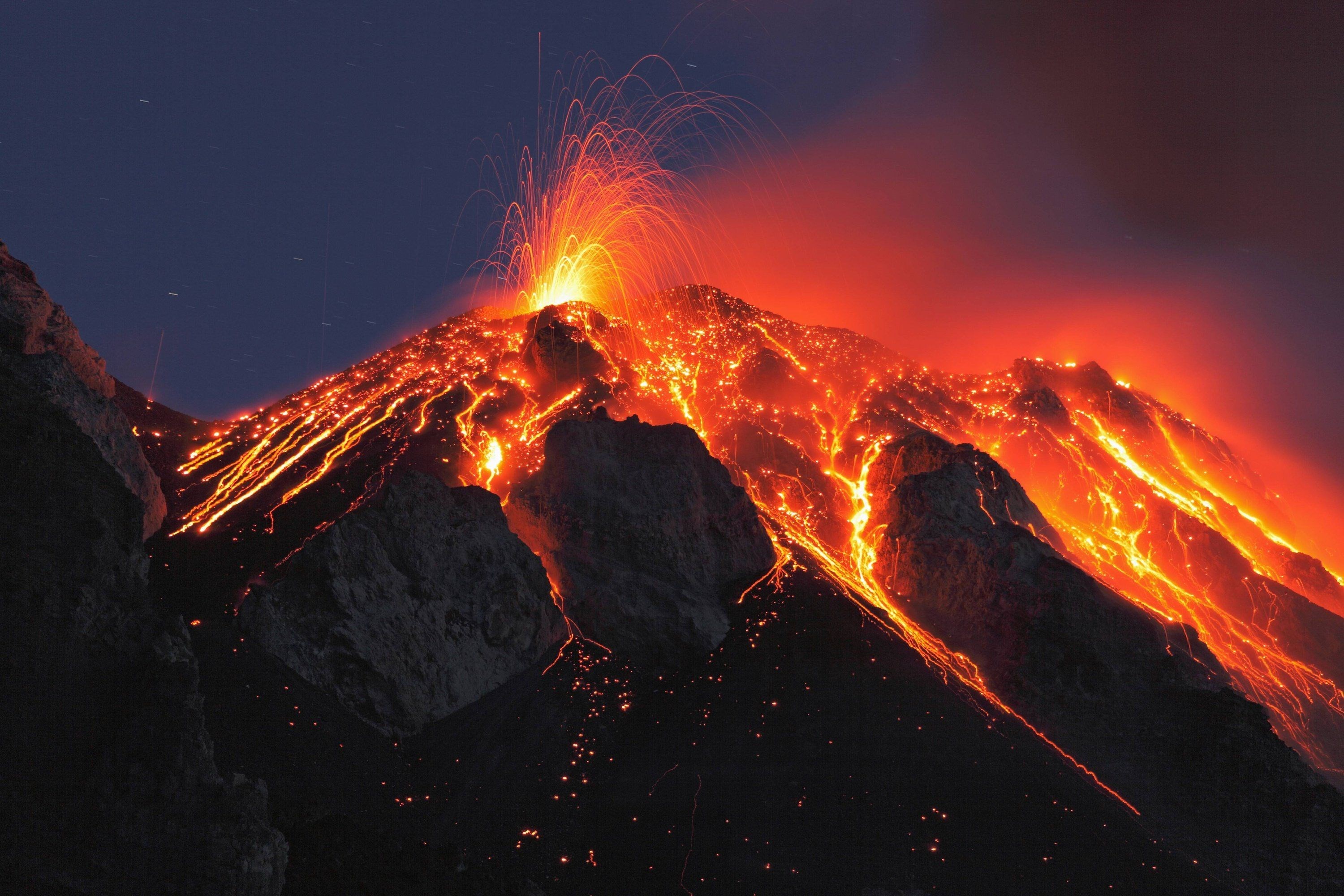 Volcano erupting with lava flows at night HD Wallpaper