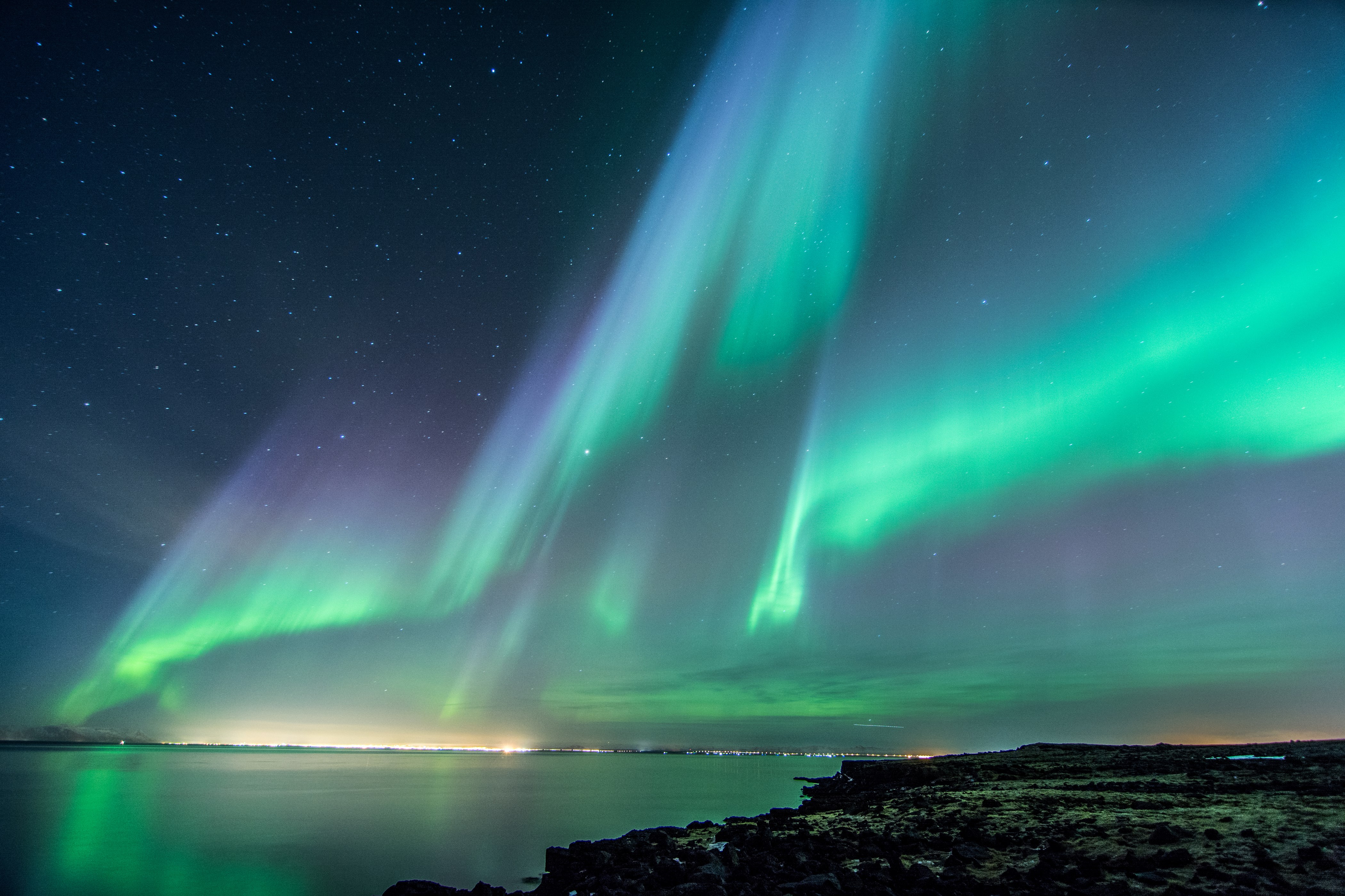 Aurora Borealis over a calm sea and rocky shore HD Wallpaper