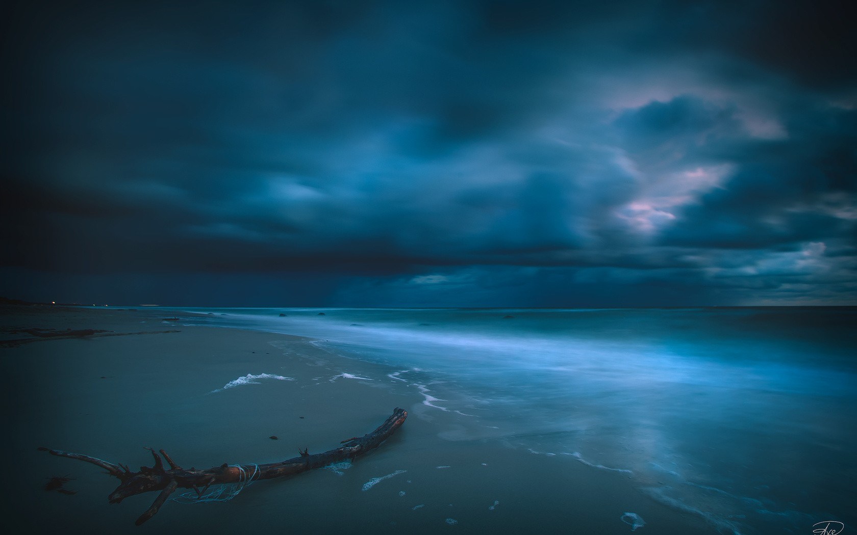 Dark stormy sky over a beach with driftwood HD Wallpaper