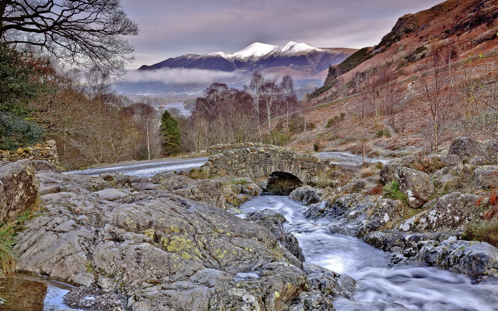 Stone bridge over a stream with snow-capped mountains in the background HD Wallpaper