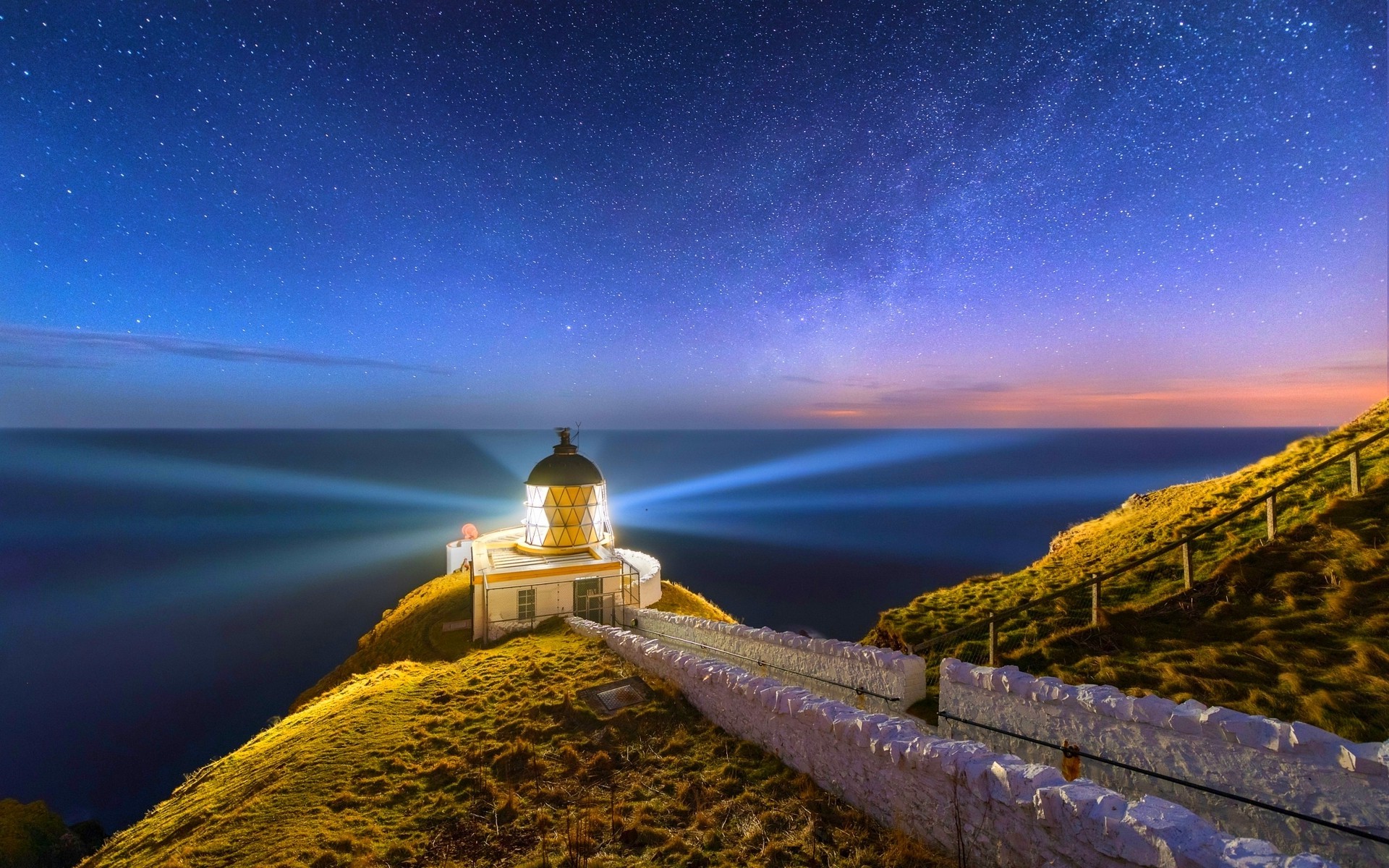 Lighthouse on a hill under a starry night sky HD Wallpaper