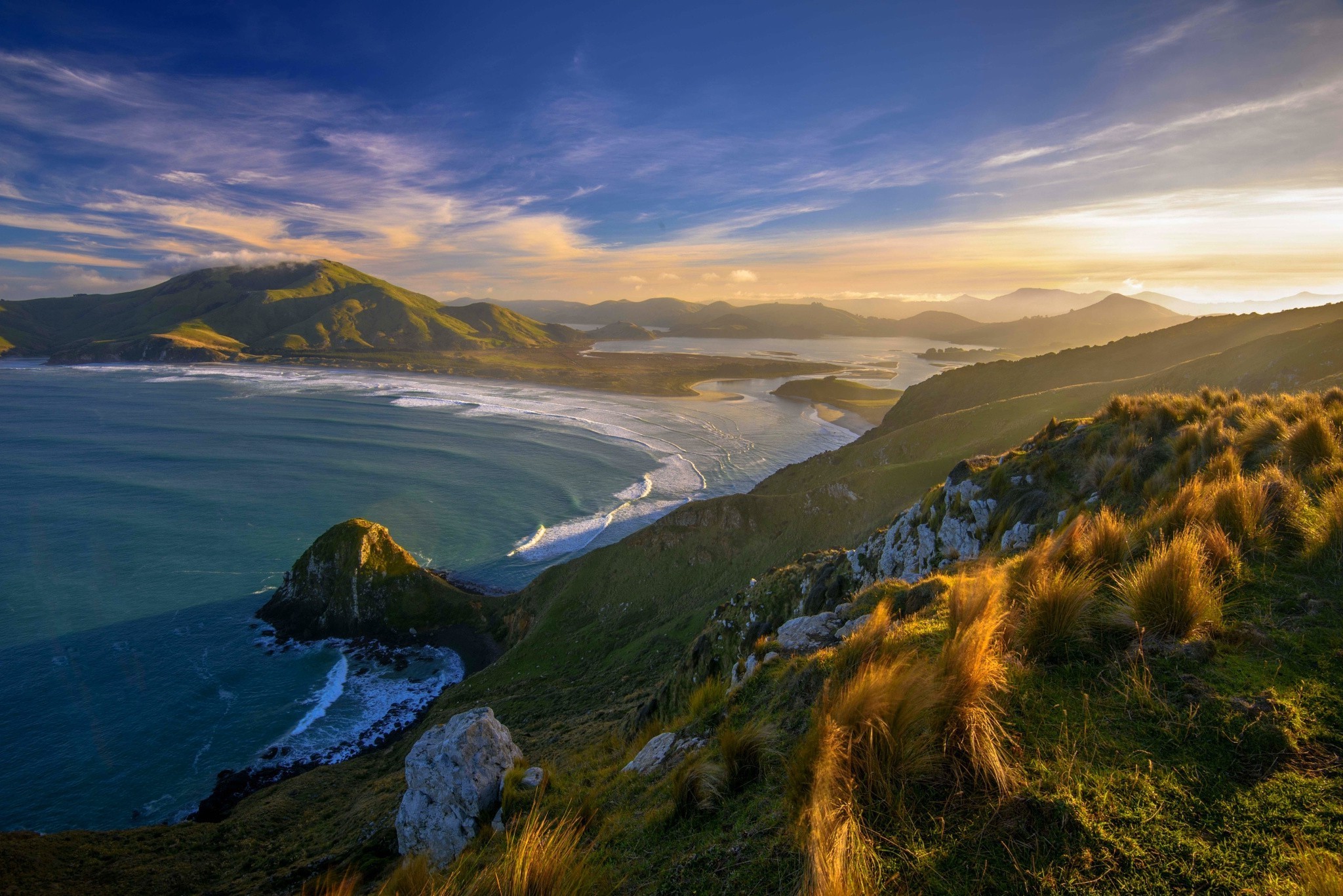 Sunset over a bay with green hills and grassy foreground HD Wallpaper
