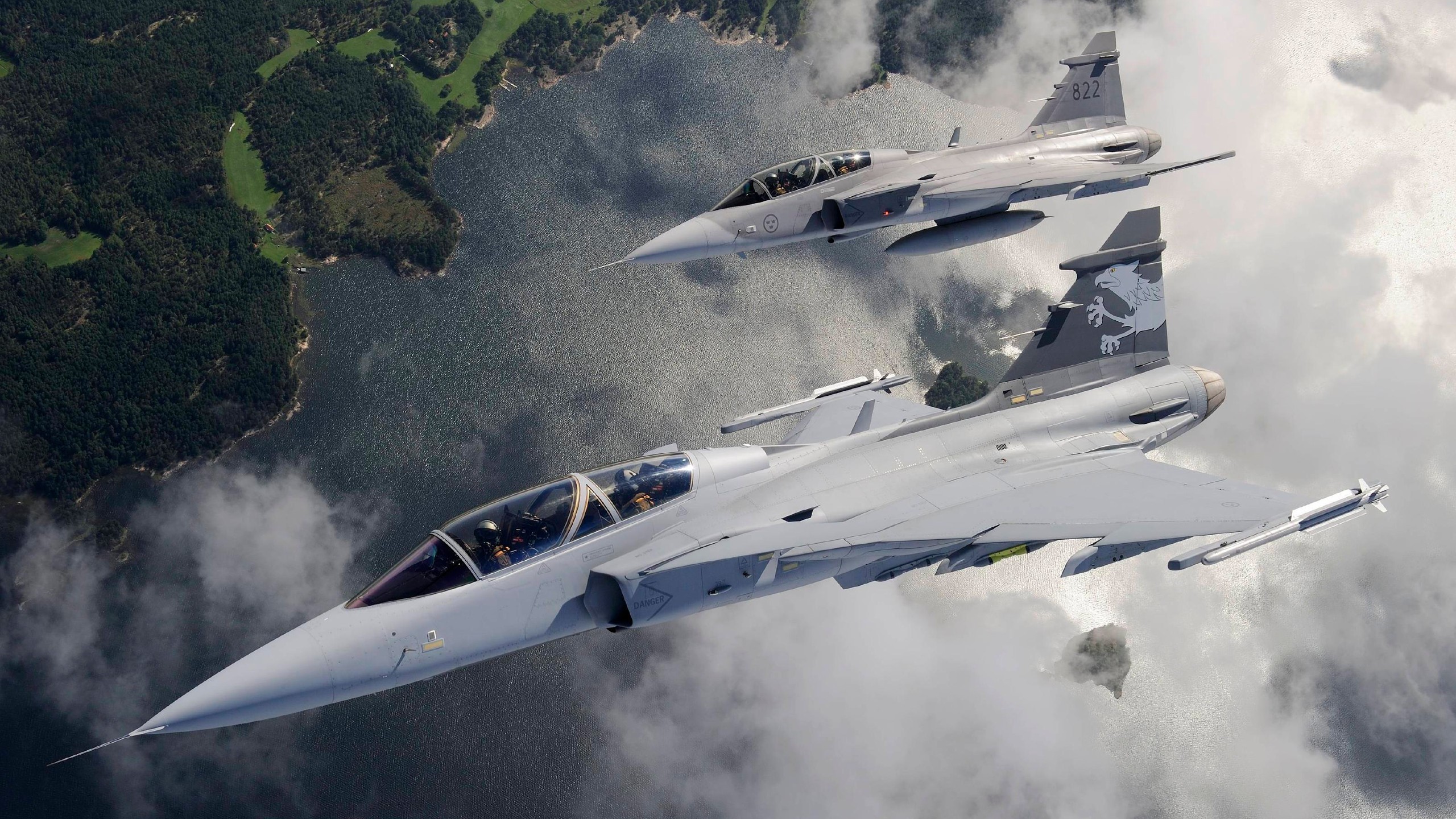 Two Swedish Air Force JAS 39 Gripen fighter jets flying over water and land HD Wallpaper