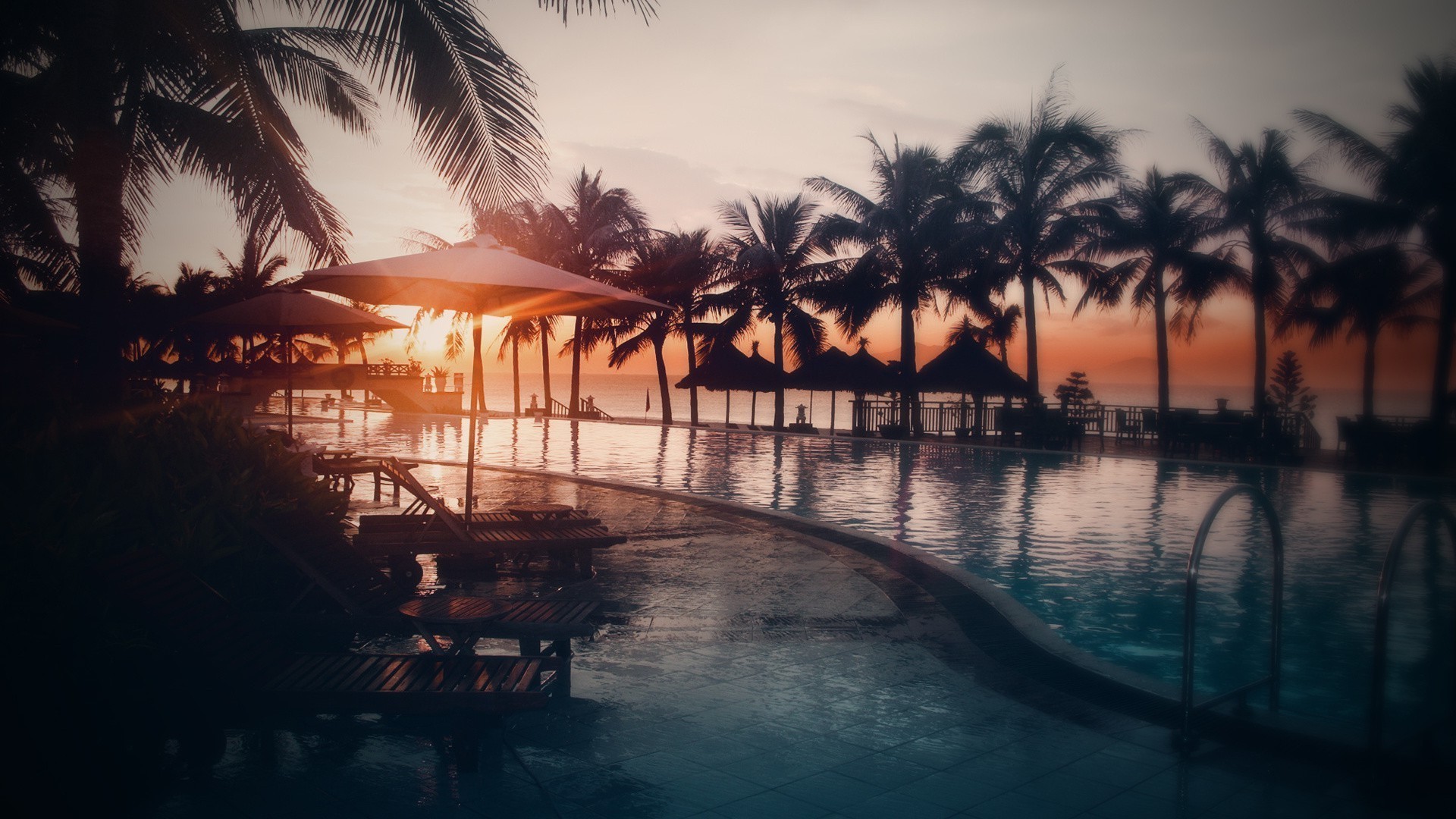 Sunset over a tropical resort with palm trees and a swimming pool HD Wallpaper