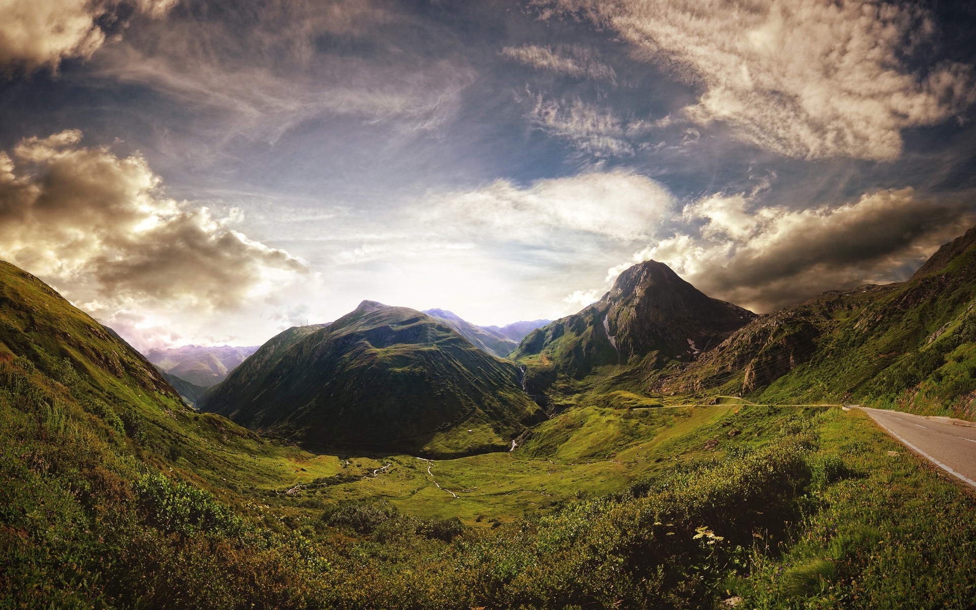 Mountain pass with a road and dramatic clouds HD Wallpaper