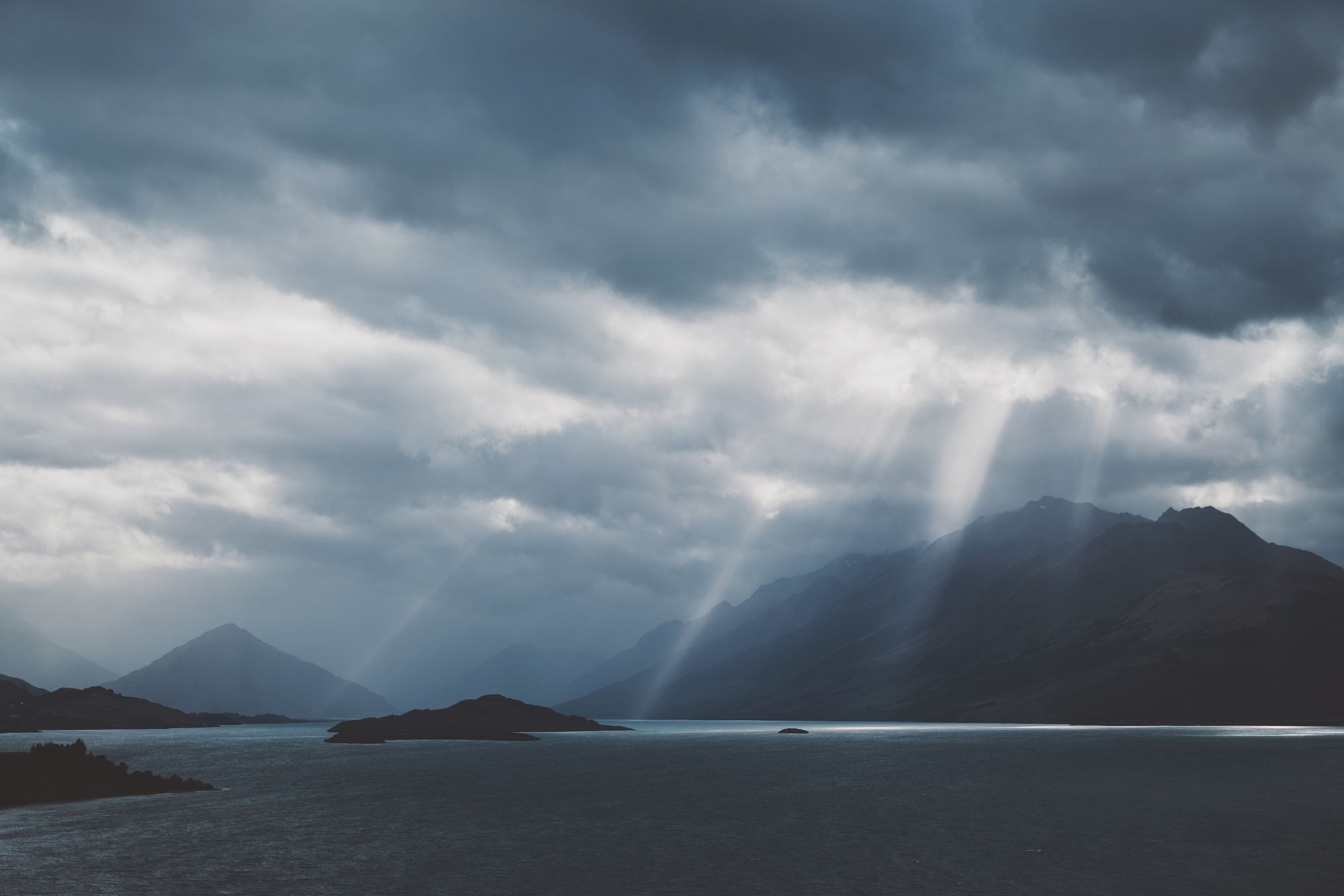 Sunbeams through clouds over mountains and a lake HD Wallpaper