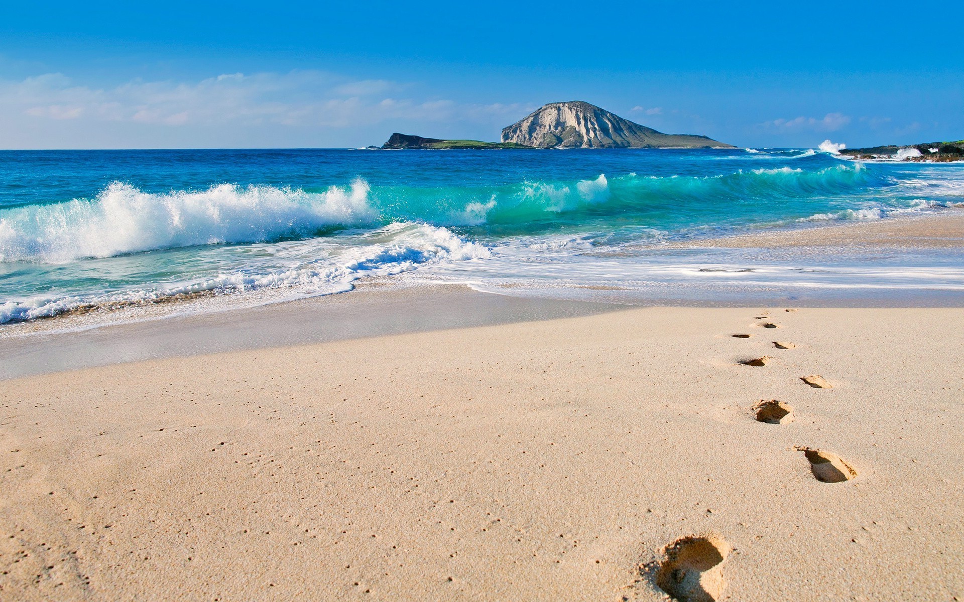 Footprints on a sandy beach with ocean waves and islands HD Wallpaper
