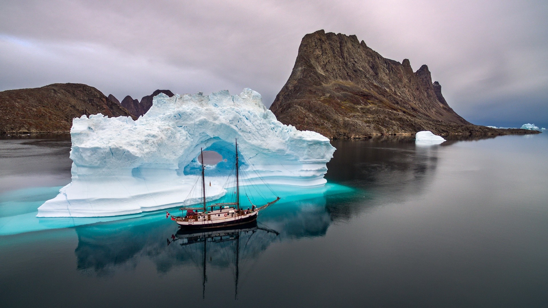 Sailing ship passes through an iceberg arch in Greenland HD Wallpaper