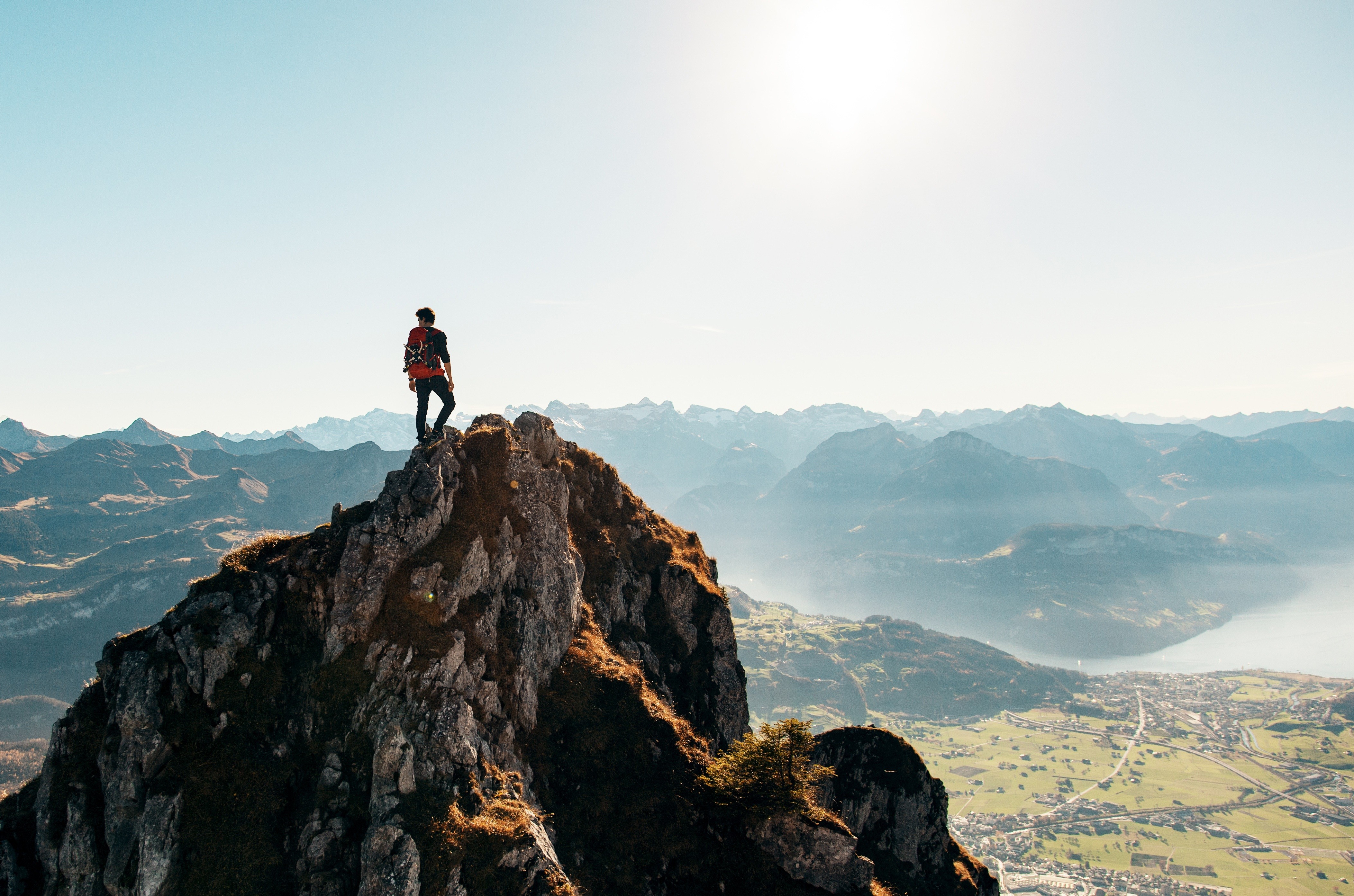 Man on mountain peak overlooking valley and lake HD Wallpaper