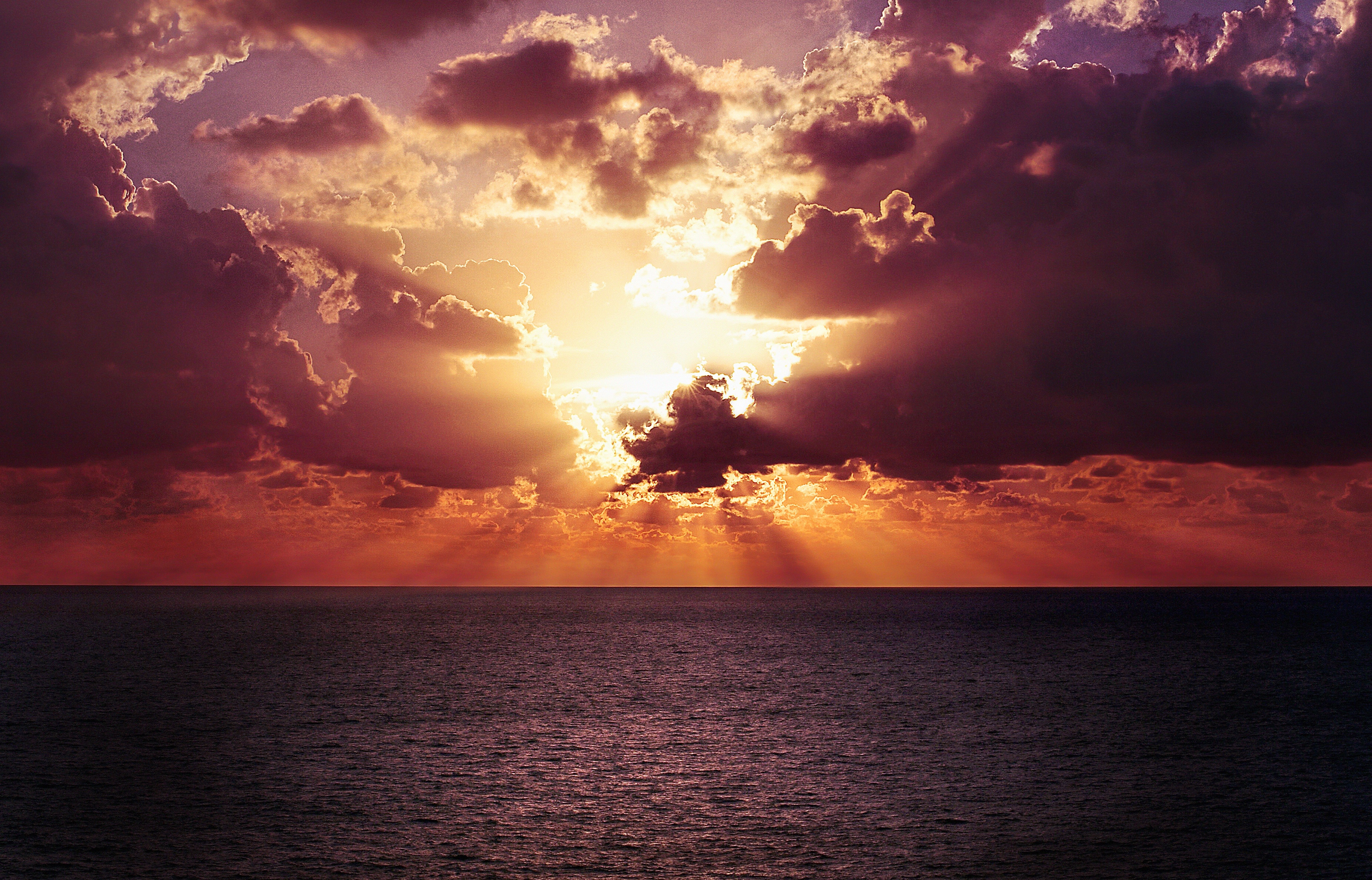 Sunset over the ocean with sun rays through clouds HD Wallpaper
