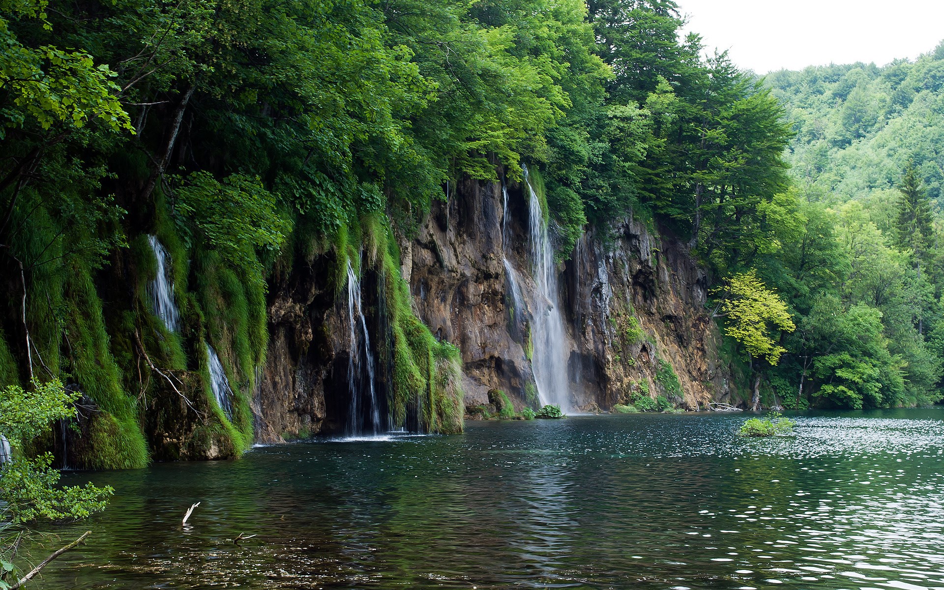 Waterfalls cascading down a rocky cliff into a lake HD Wallpaper