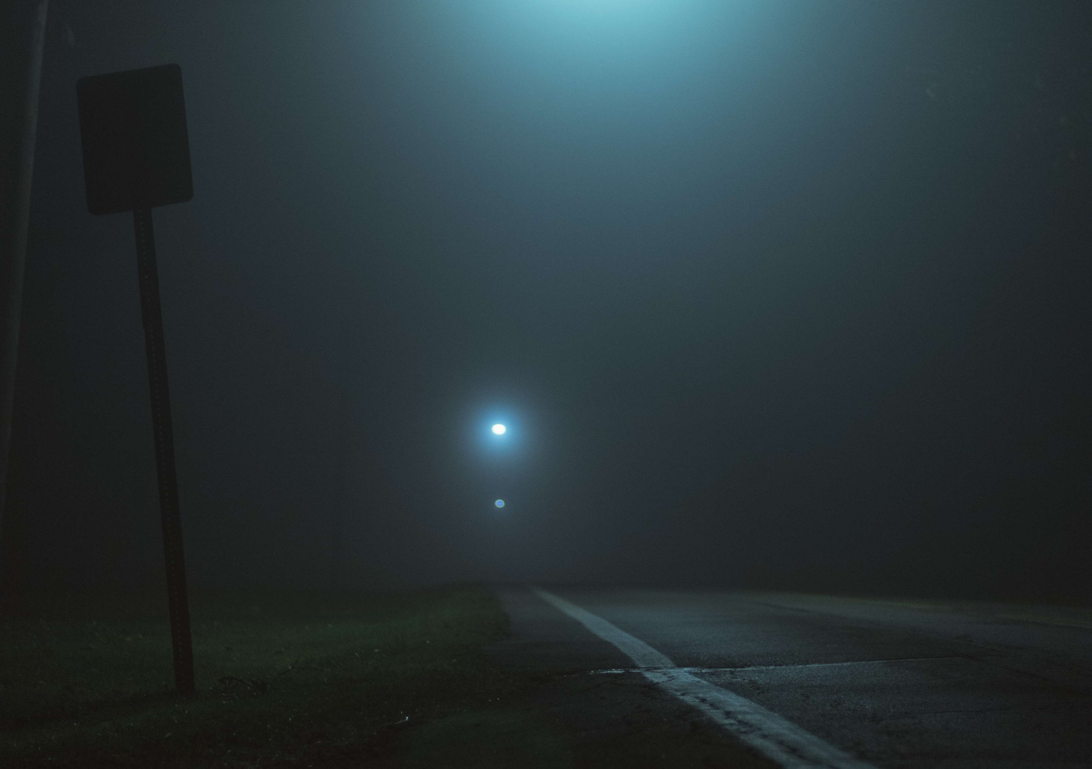 Foggy road at night with streetlights and a sign HD Wallpaper