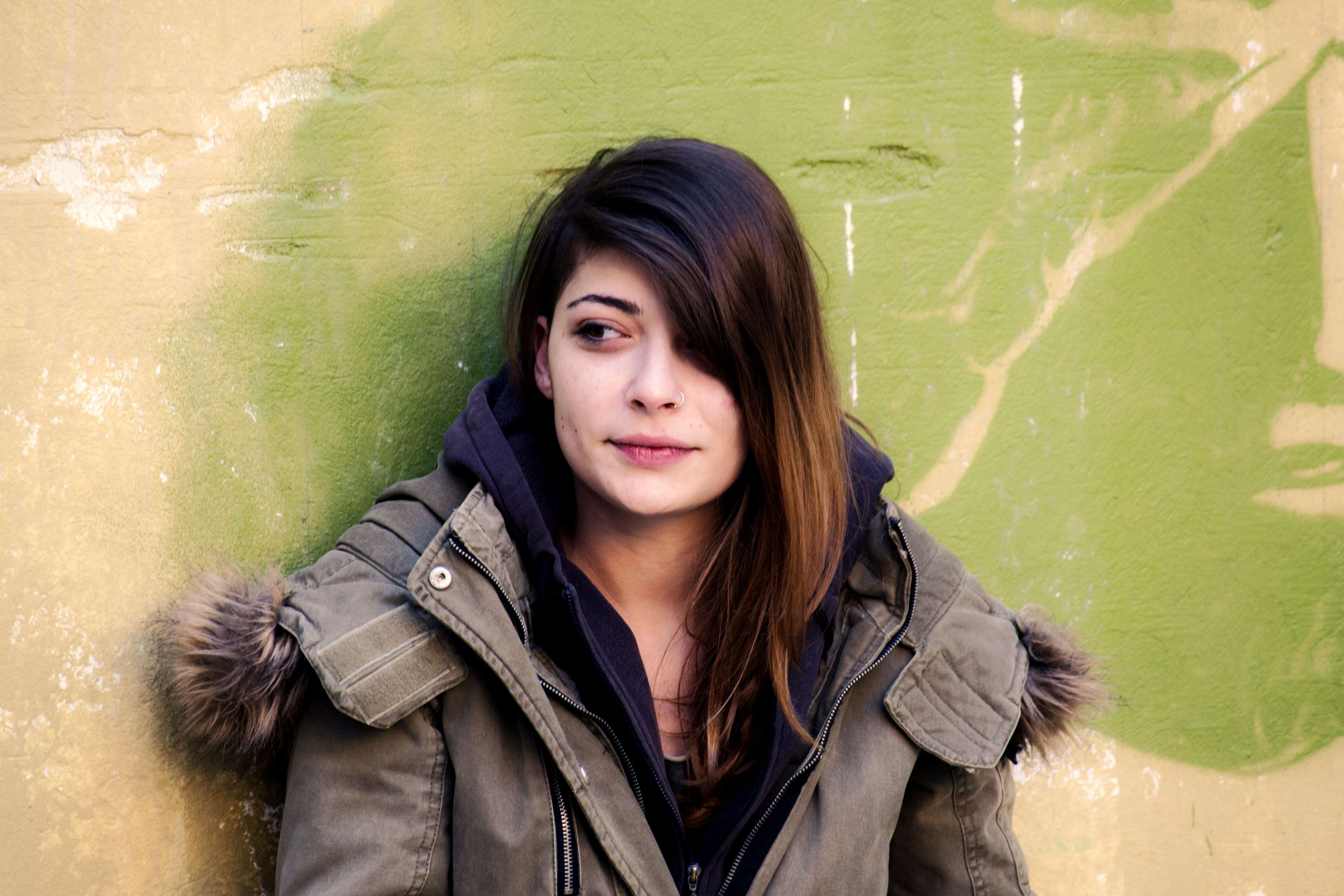 Young woman in a jacket leaning against a wall HD Wallpaper