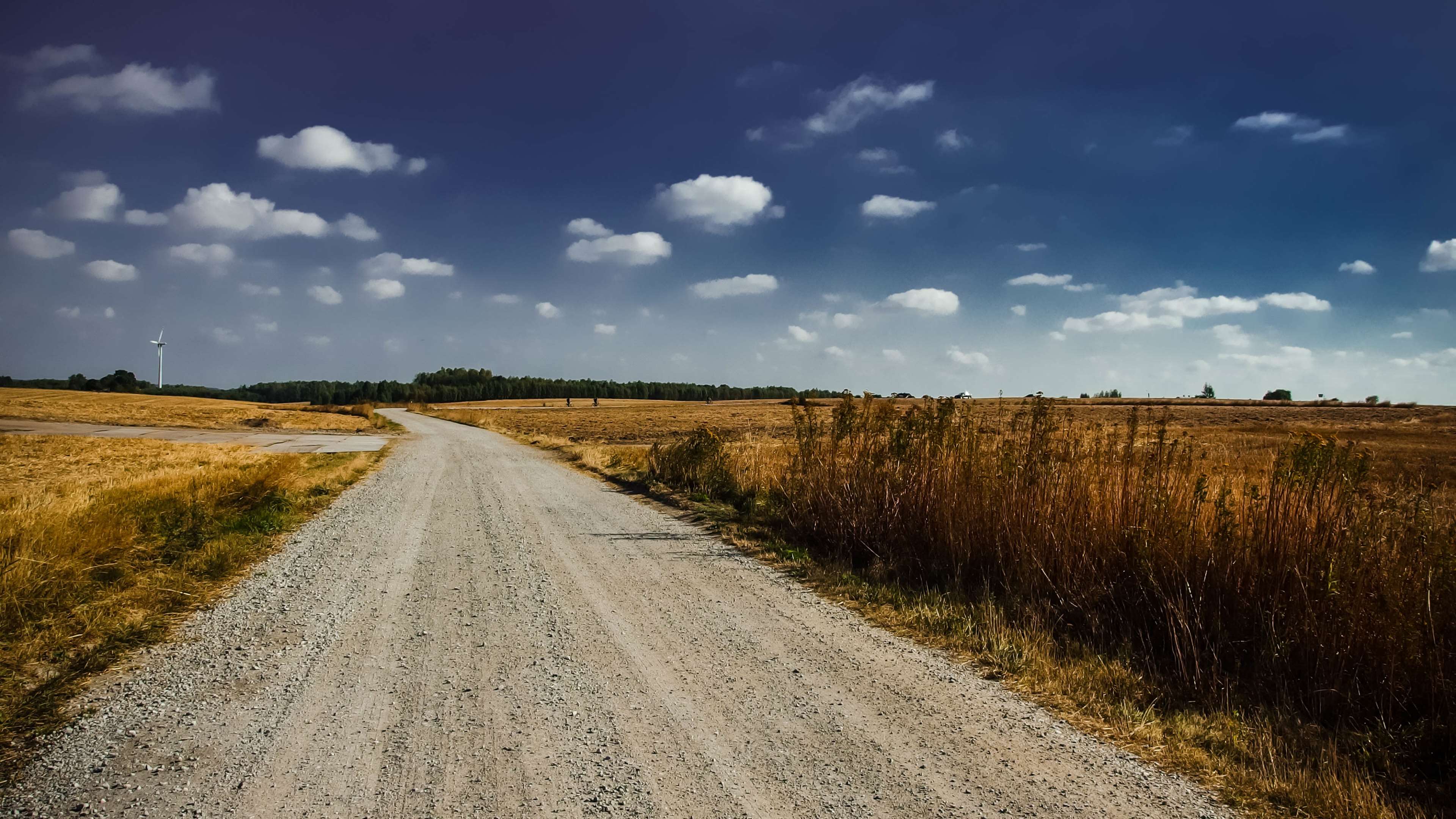 Dirt road through fields with windmill under cloudy sky HD Wallpaper