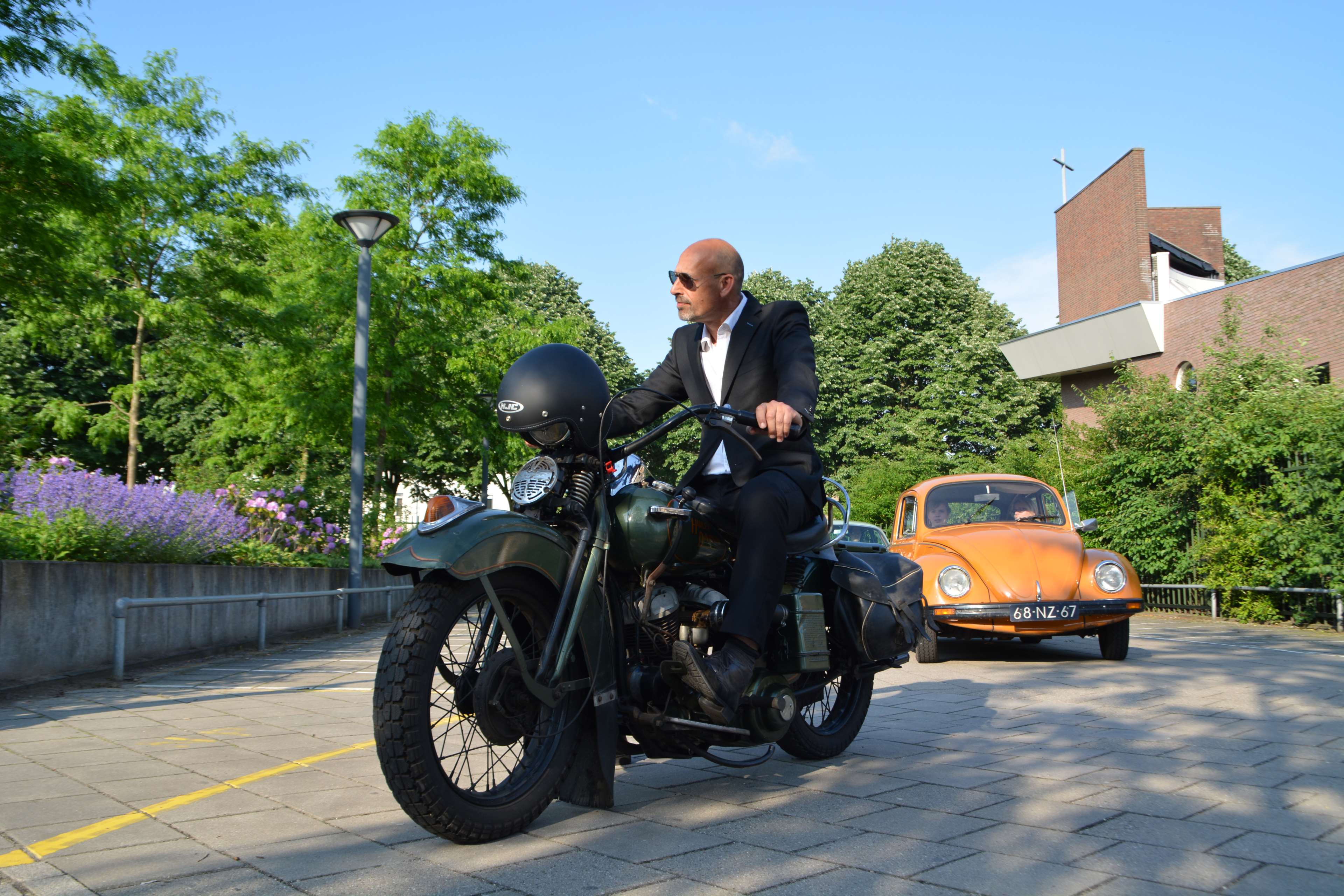 Man in suit riding Harley Davidson motorcycle with orange Beetle car HD Wallpaper