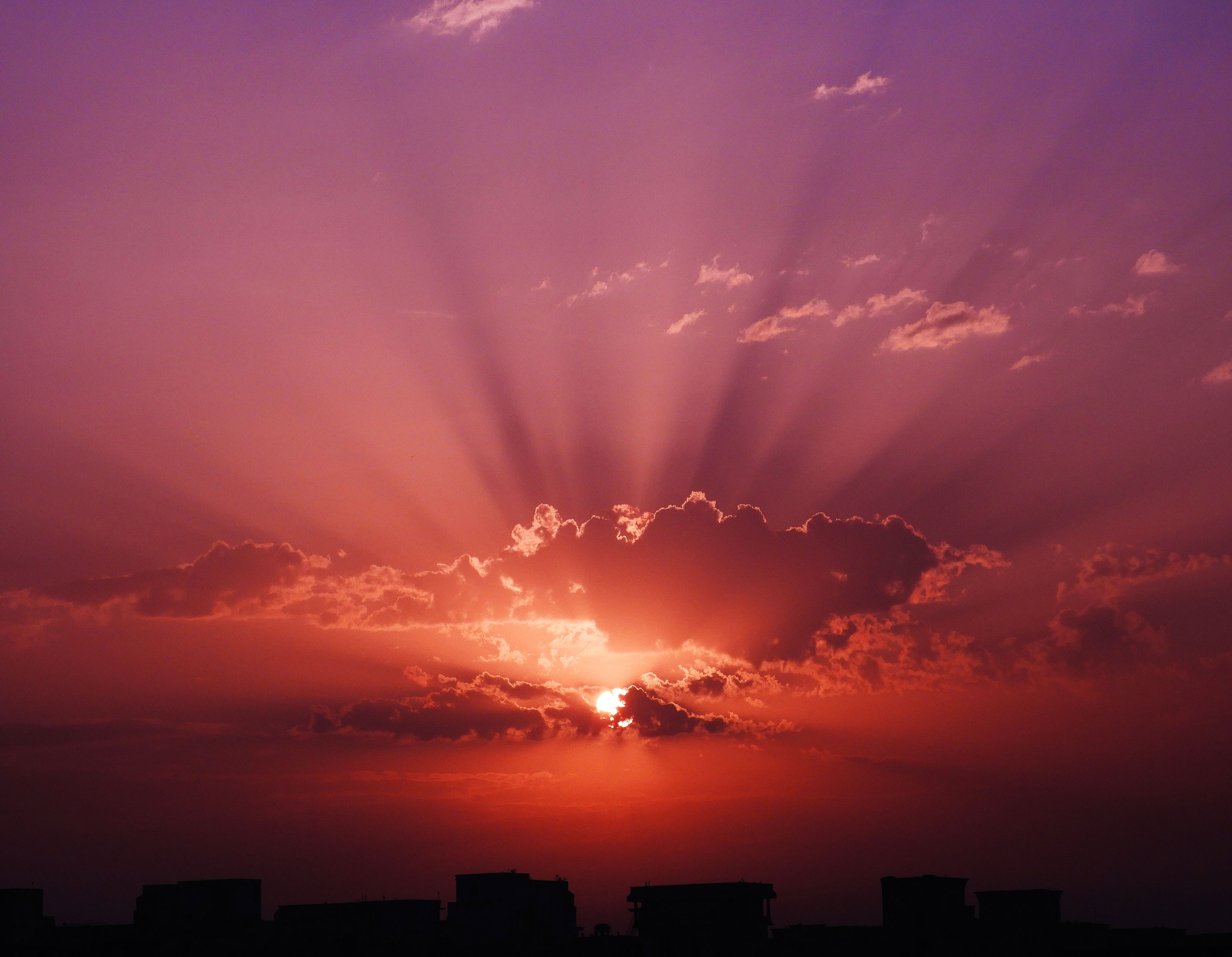 Sunset with crepuscular rays over city skyline HD Wallpaper