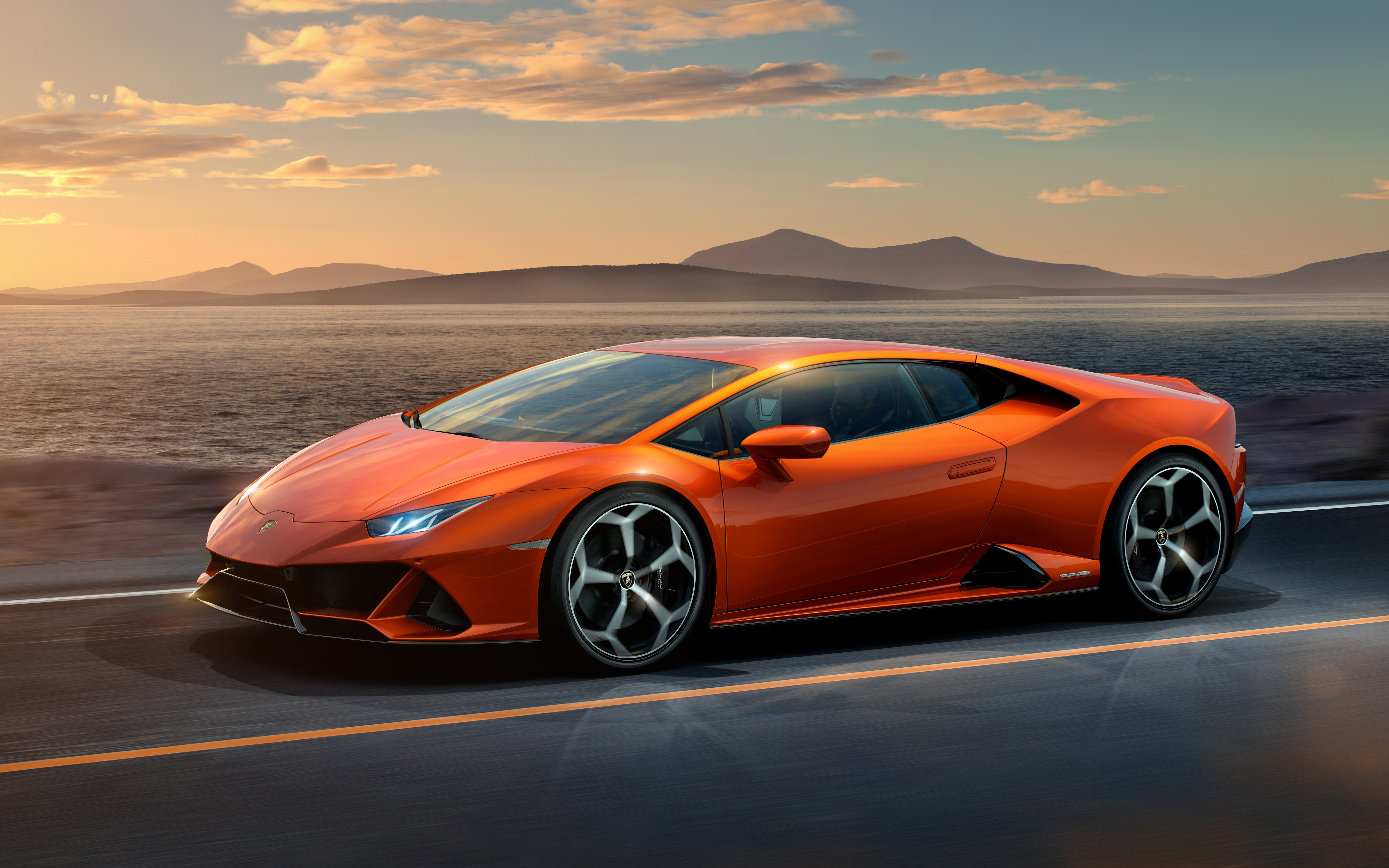Orange Lamborghini Huracan driving on a road by the sea HD Wallpaper