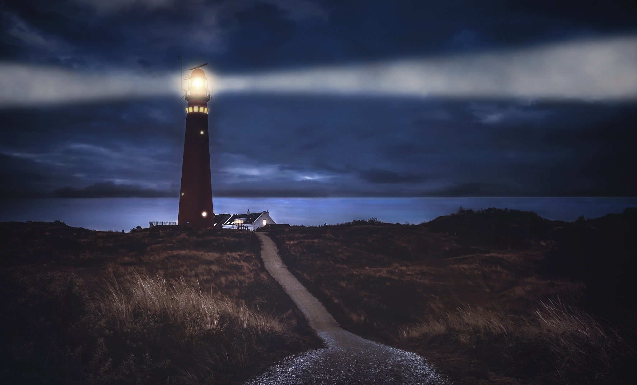 Lighthouse shining light on the sea at night HD Wallpaper