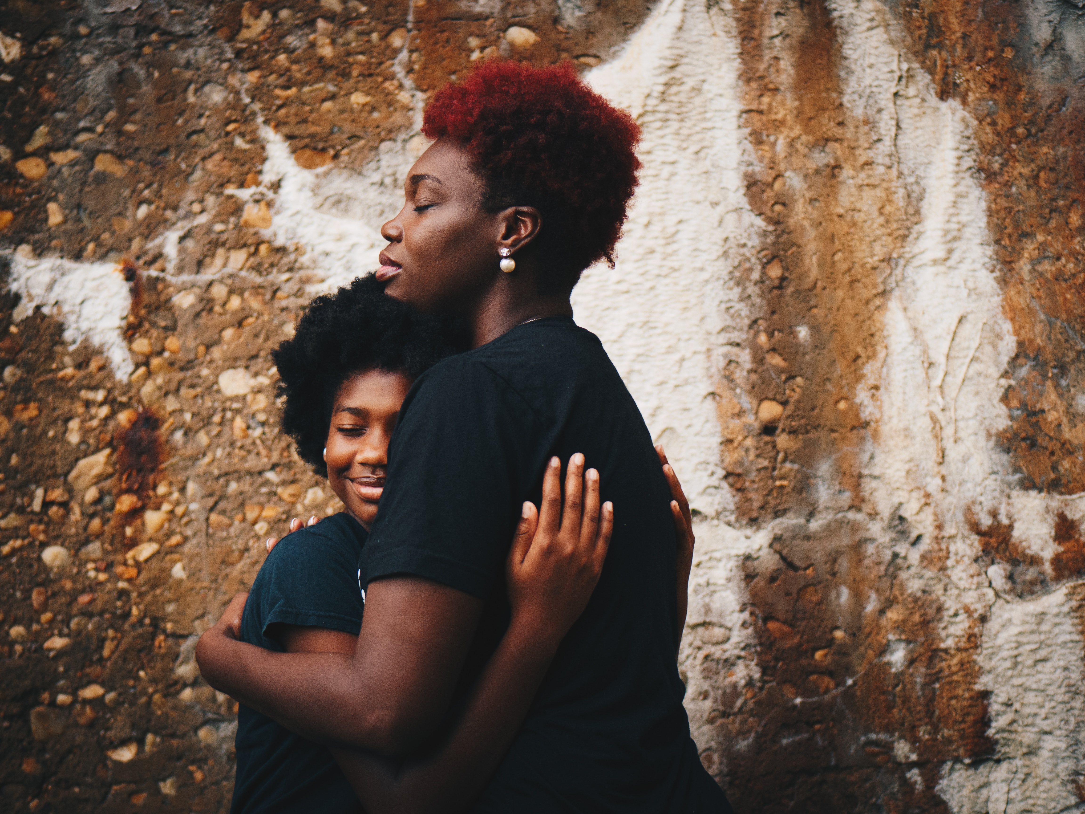 Two African American women hugging in front of a stone wall HD Wallpaper