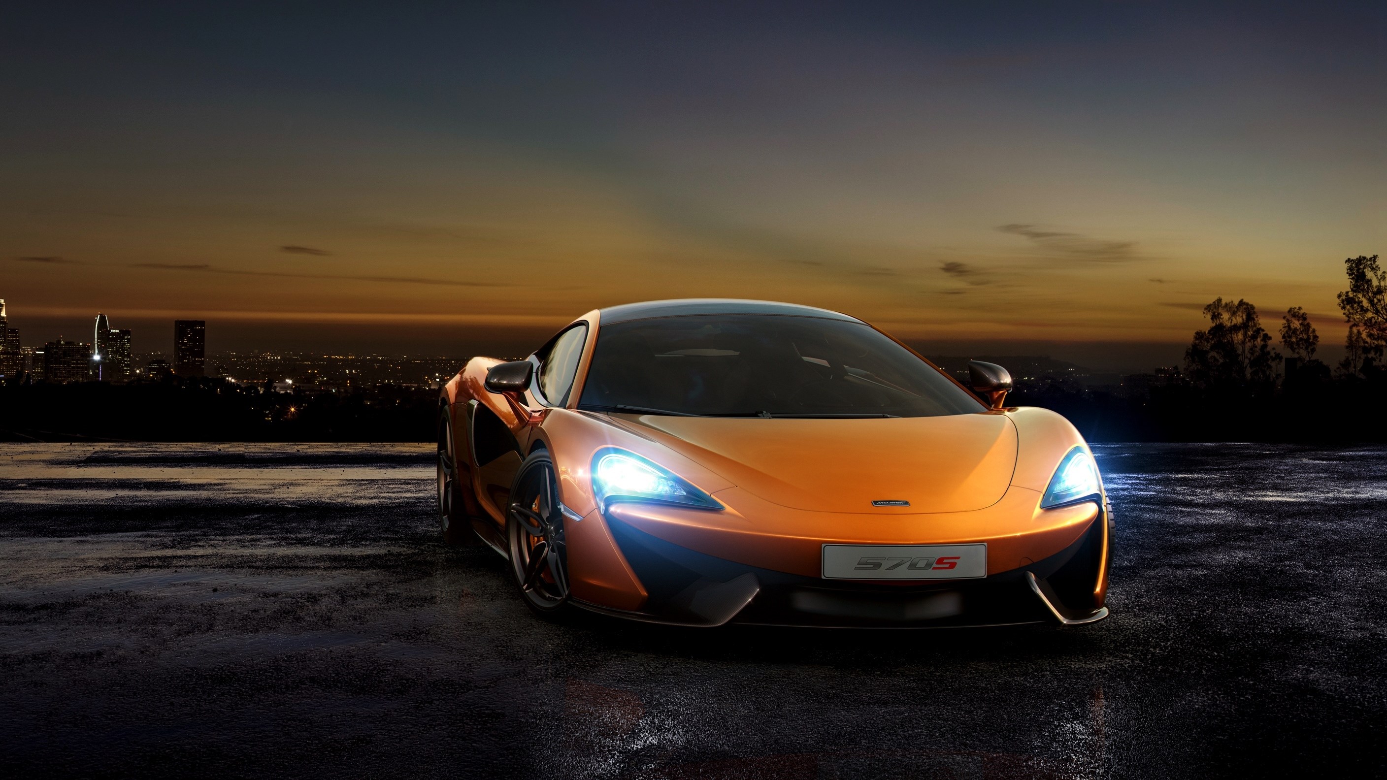 Orange McLaren 570S parked at dusk with city skyline HD Wallpaper