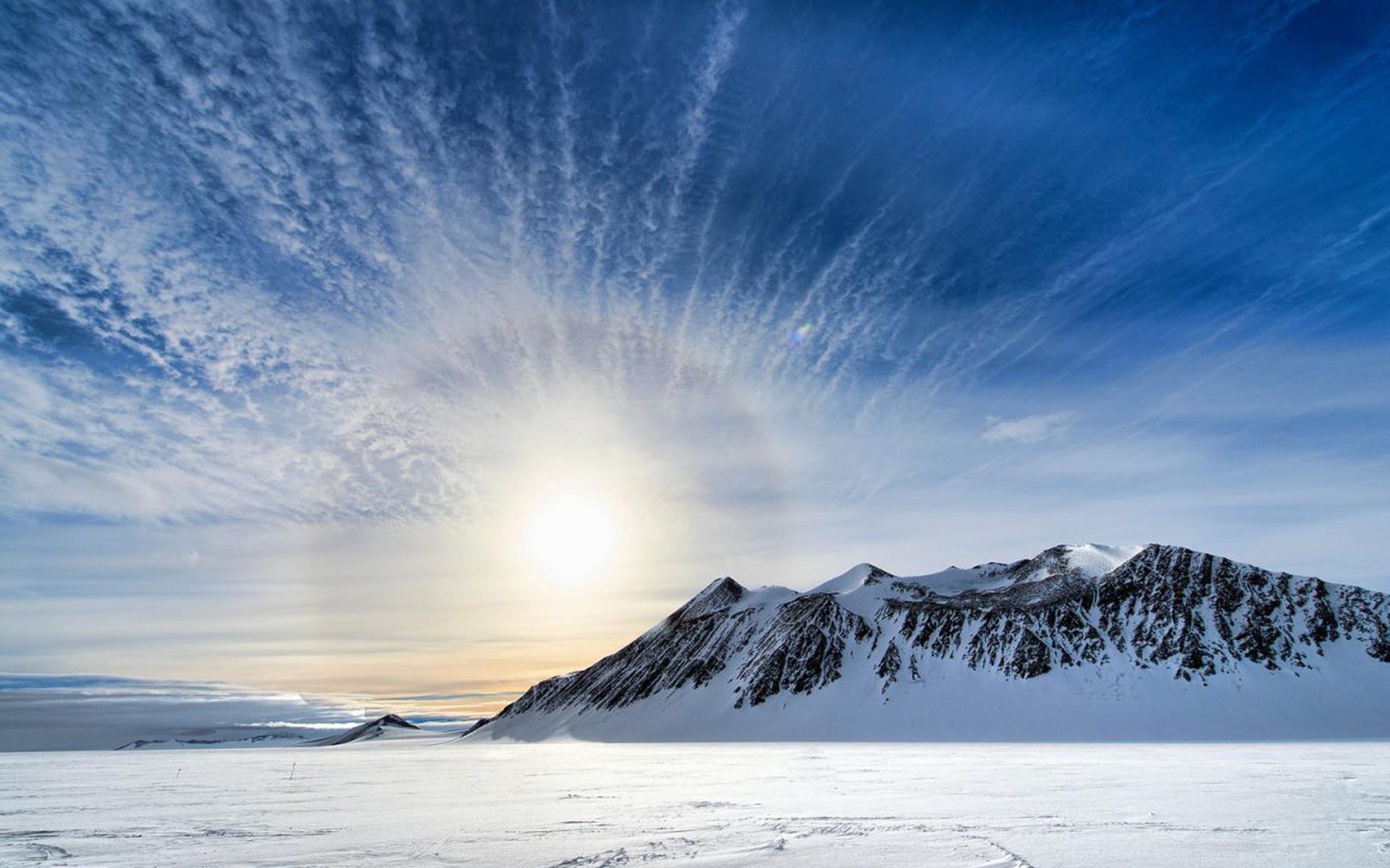 Snowy mountains under a haloed sun and cloudy sky HD Wallpaper