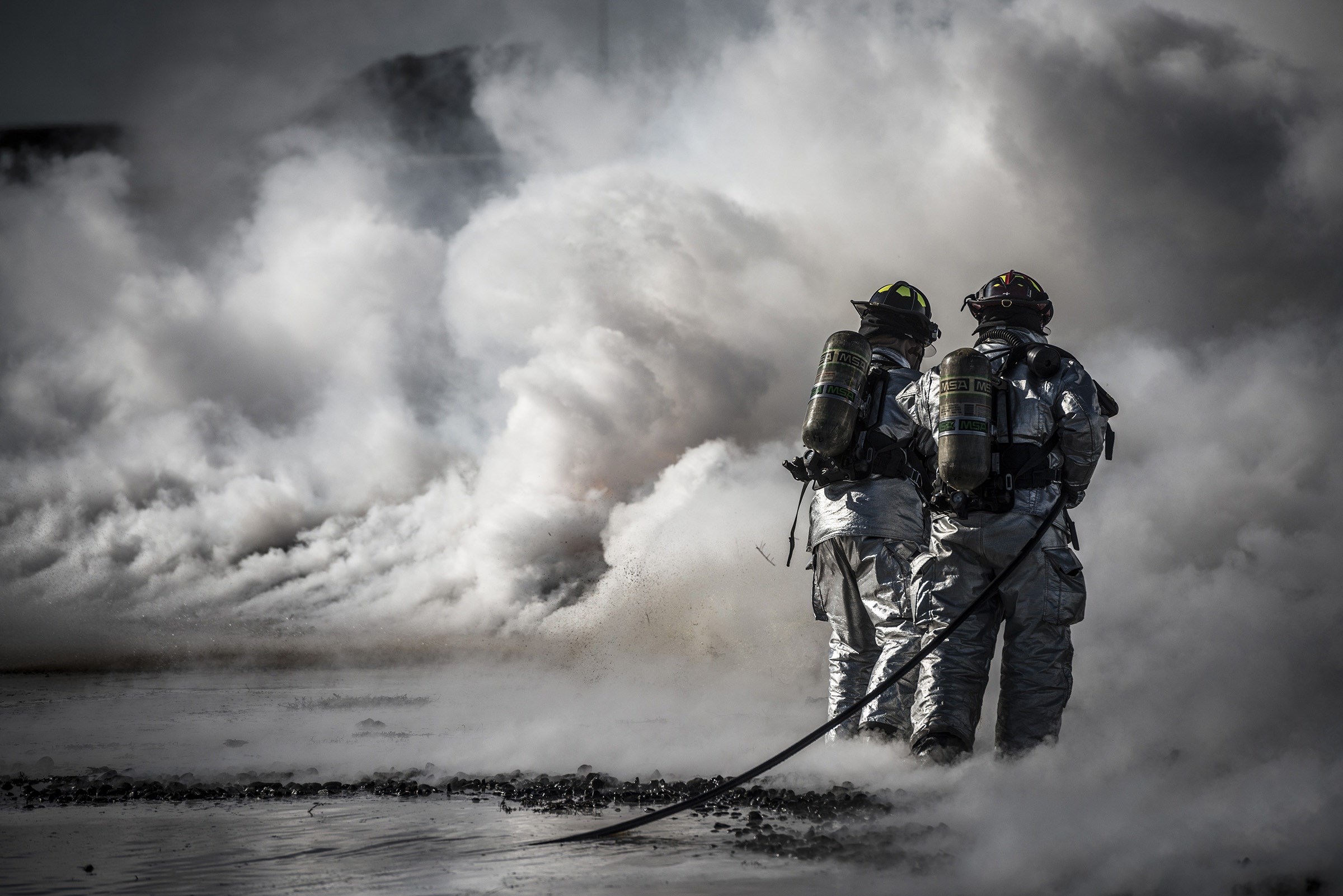 Two firefighters in protective gear amidst smoke HD Wallpaper