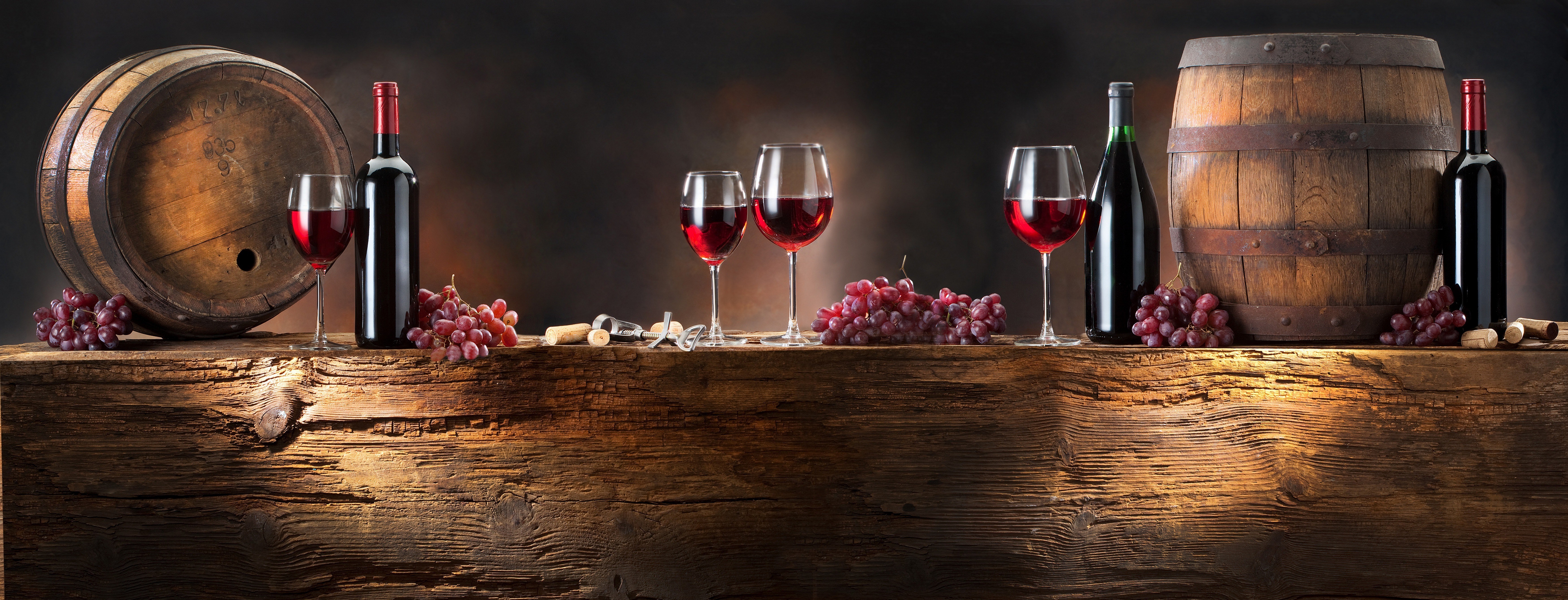 Wine bottles, glasses, grapes, and barrels on a wooden table HD Wallpaper