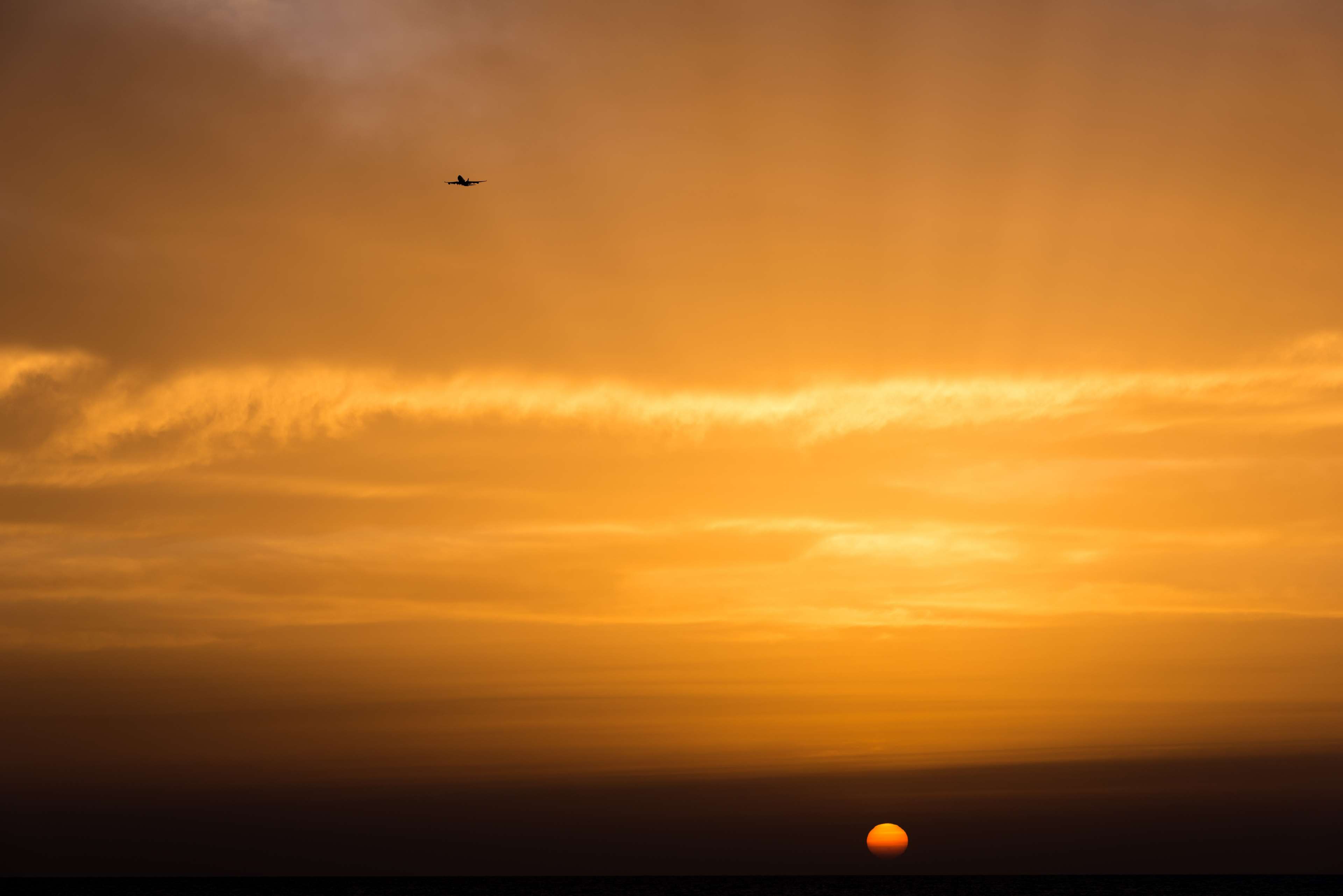 Airplane flying in orange sunset sky with clouds HD Wallpaper