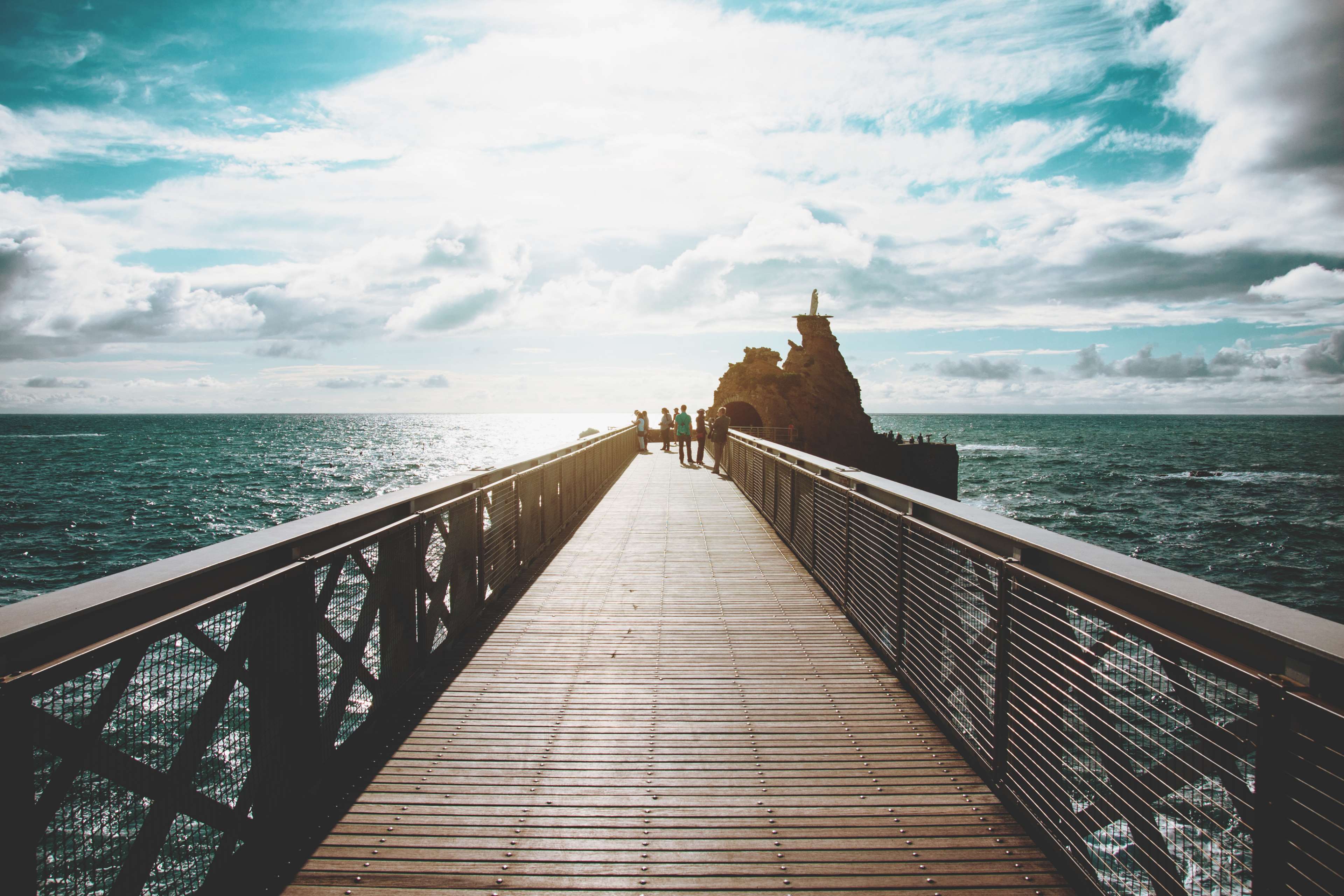 Wooden pier leading to a rocky outcrop in the ocean HD Wallpaper