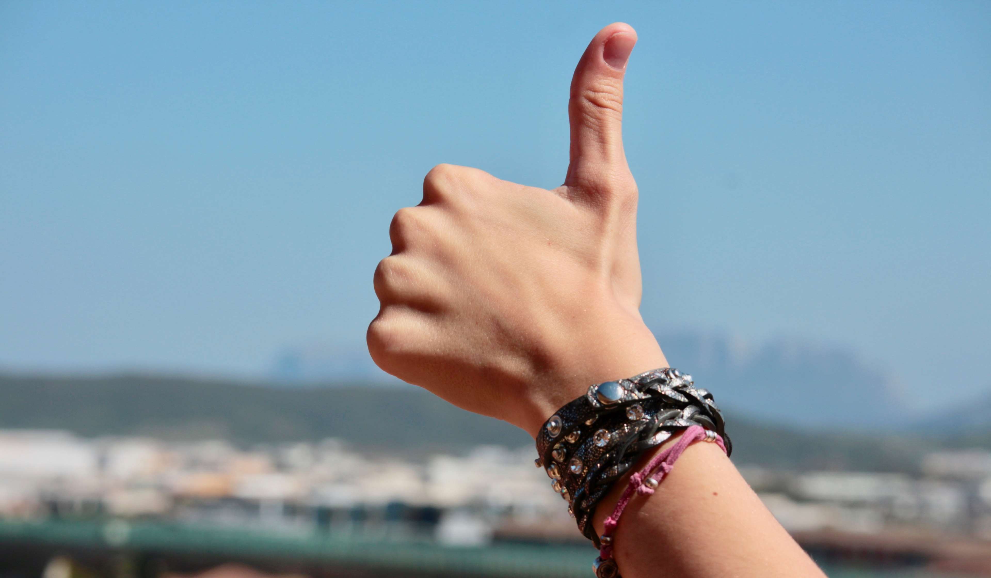 Hand with bracelets giving thumbs up HD Wallpaper