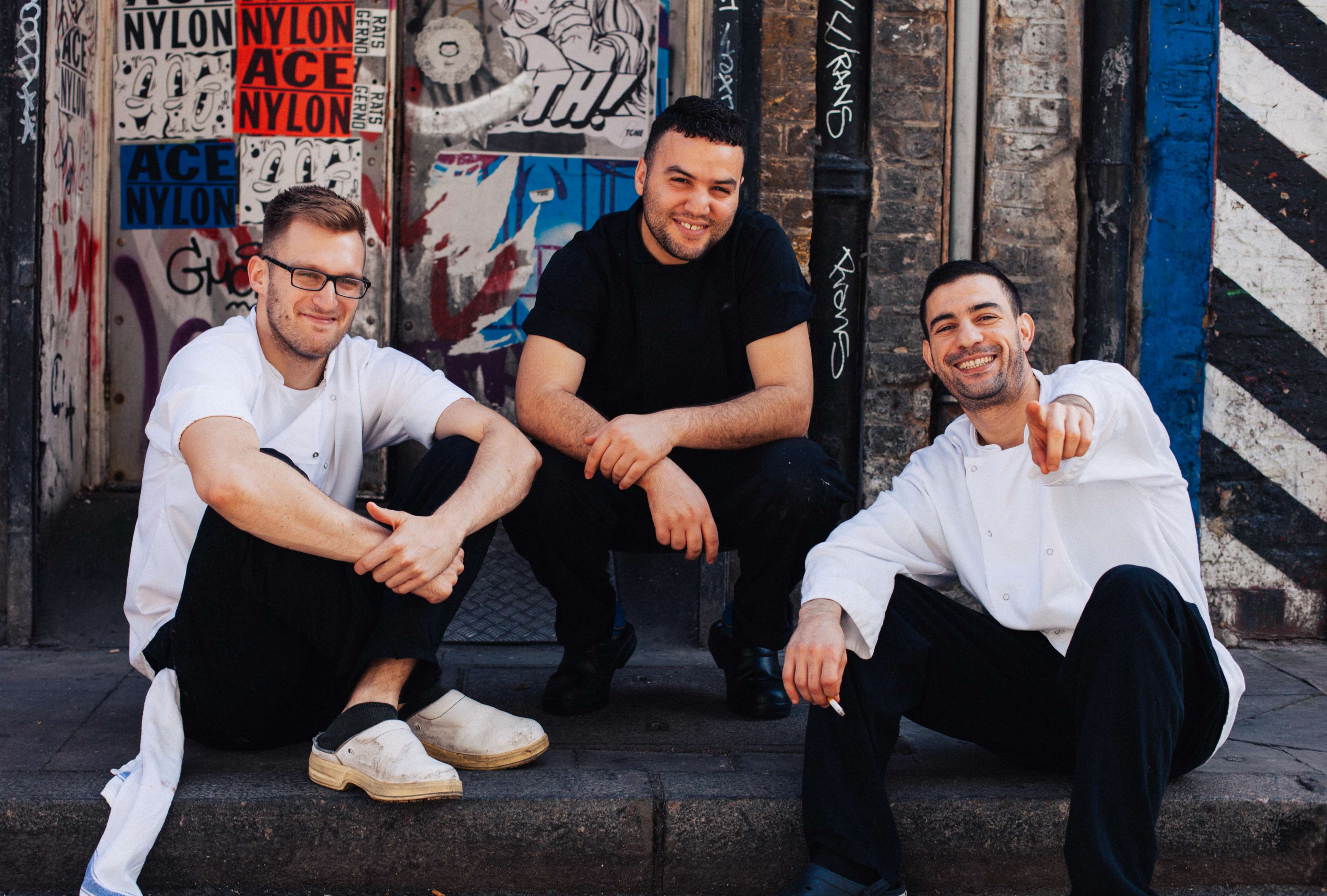 Three men in chef attire posing on a city street HD Wallpaper