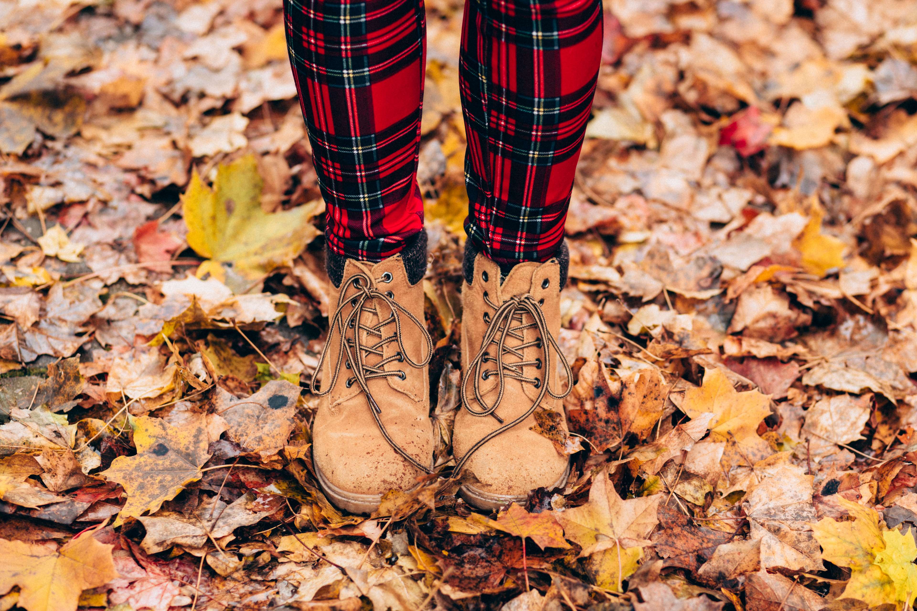 Person wearing plaid leggings and boots in autumn leaves 4K HD Wallpaper