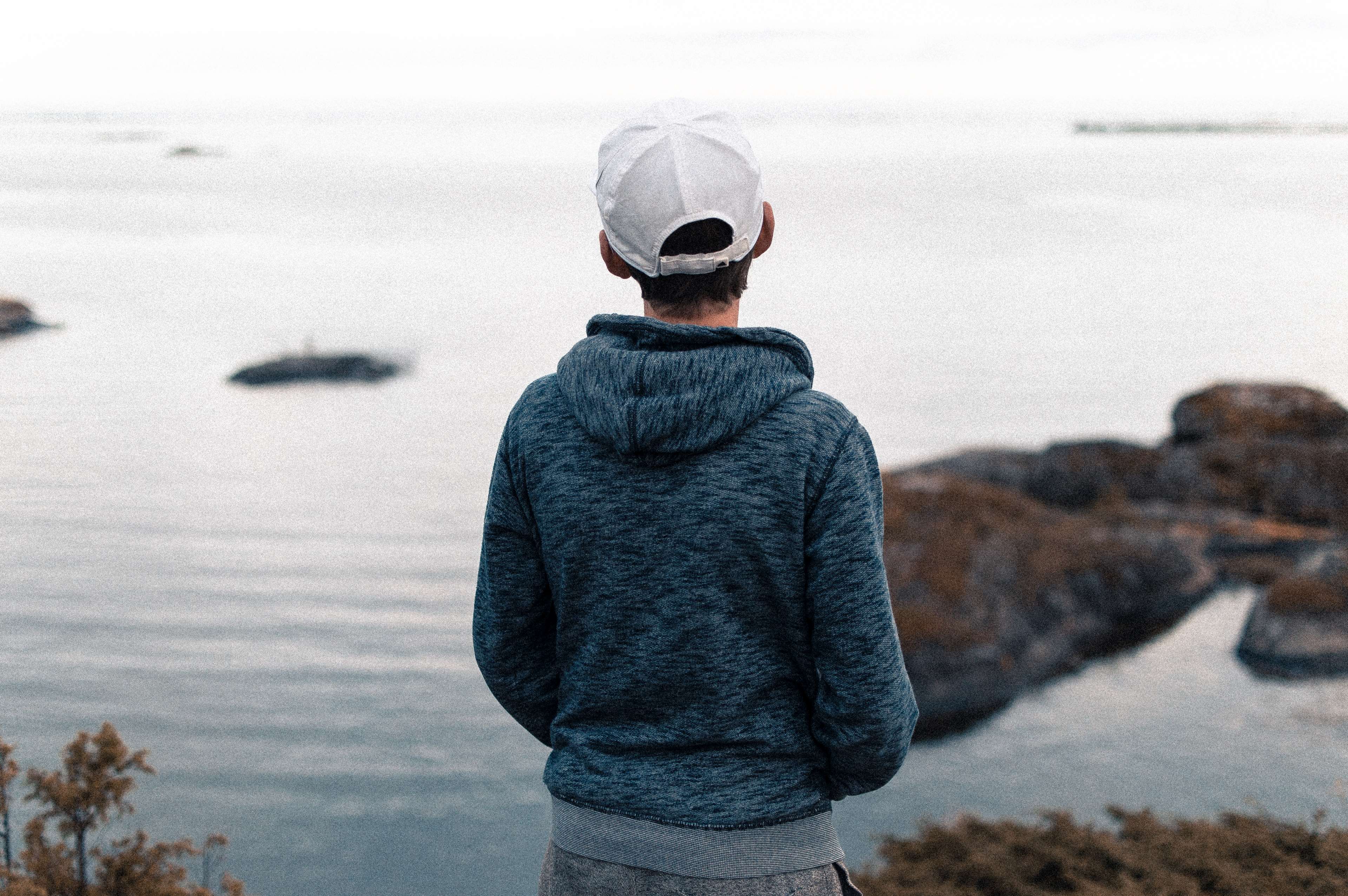 Person wearing a hoodie and cap looking at the sea HD Wallpaper