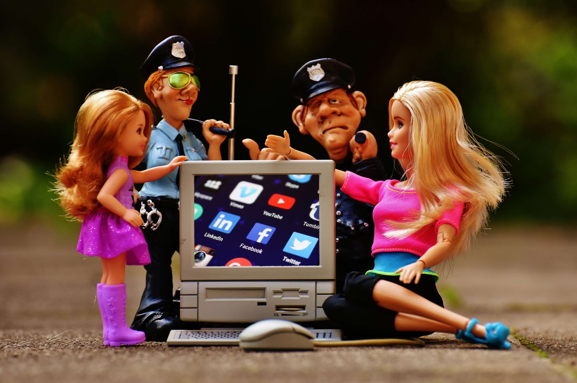 Dolls and police figures interact with a computer displaying social media icons HD Wallpaper