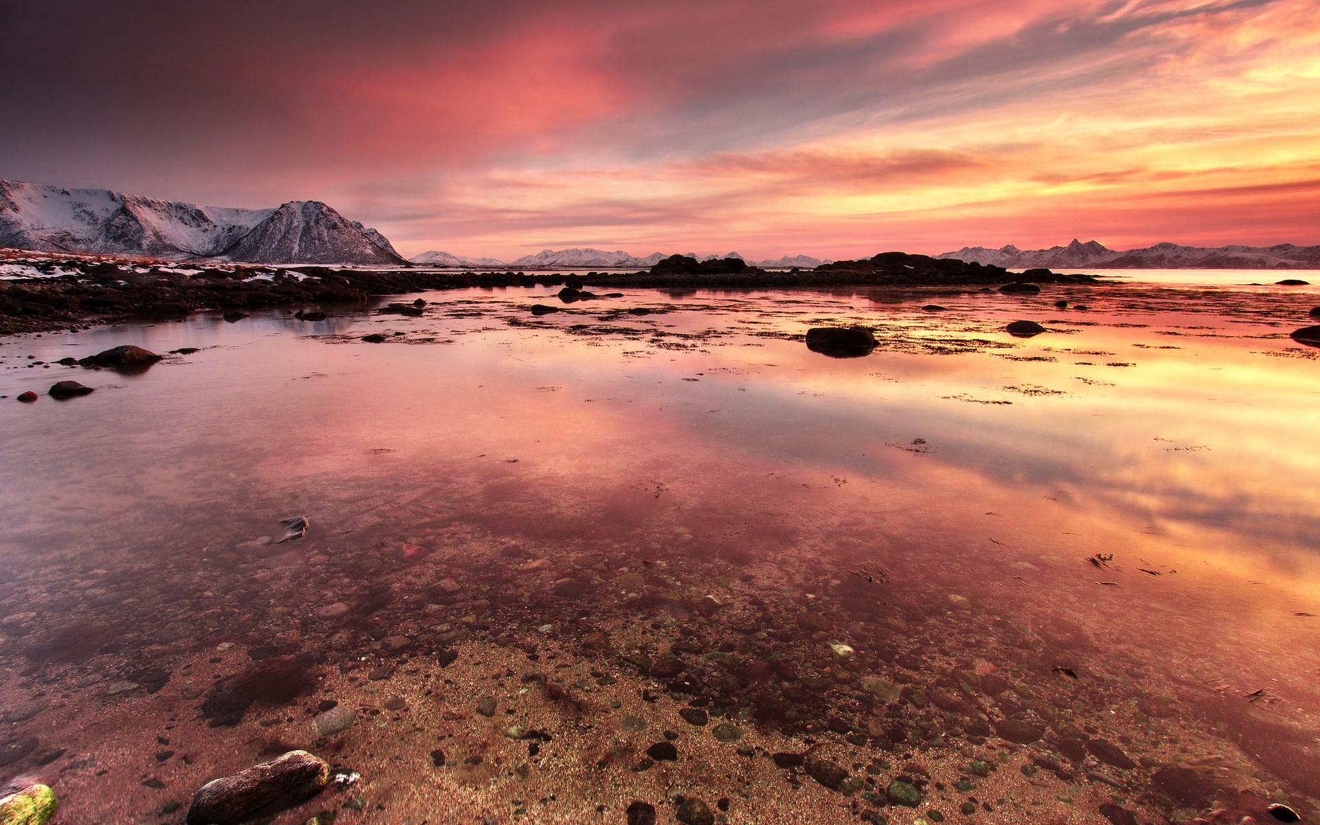 Sunset over a rocky coastline with snow-capped mountains HD Wallpaper