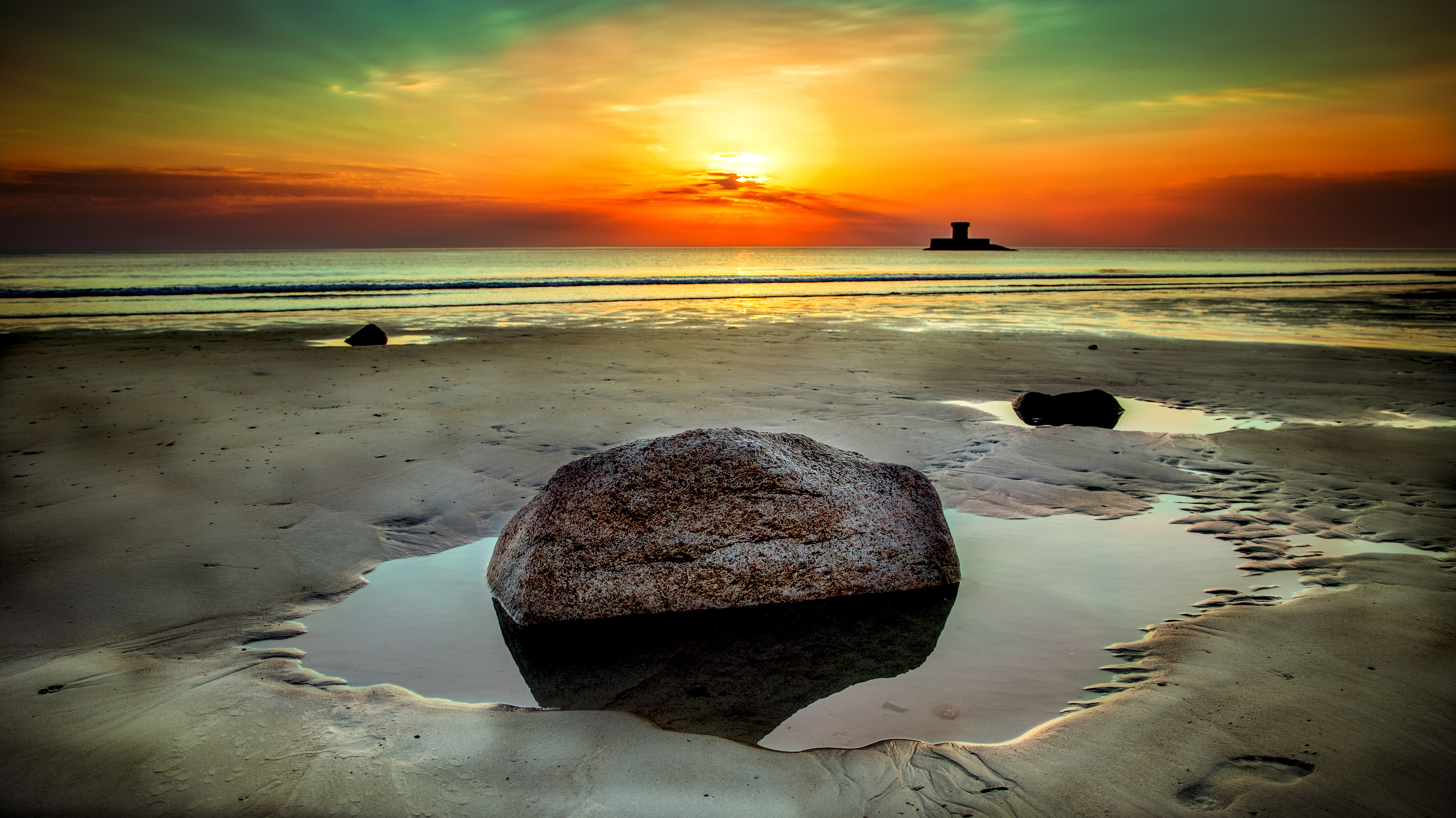 Beach sunset with rocks and a distant tower HD Wallpaper