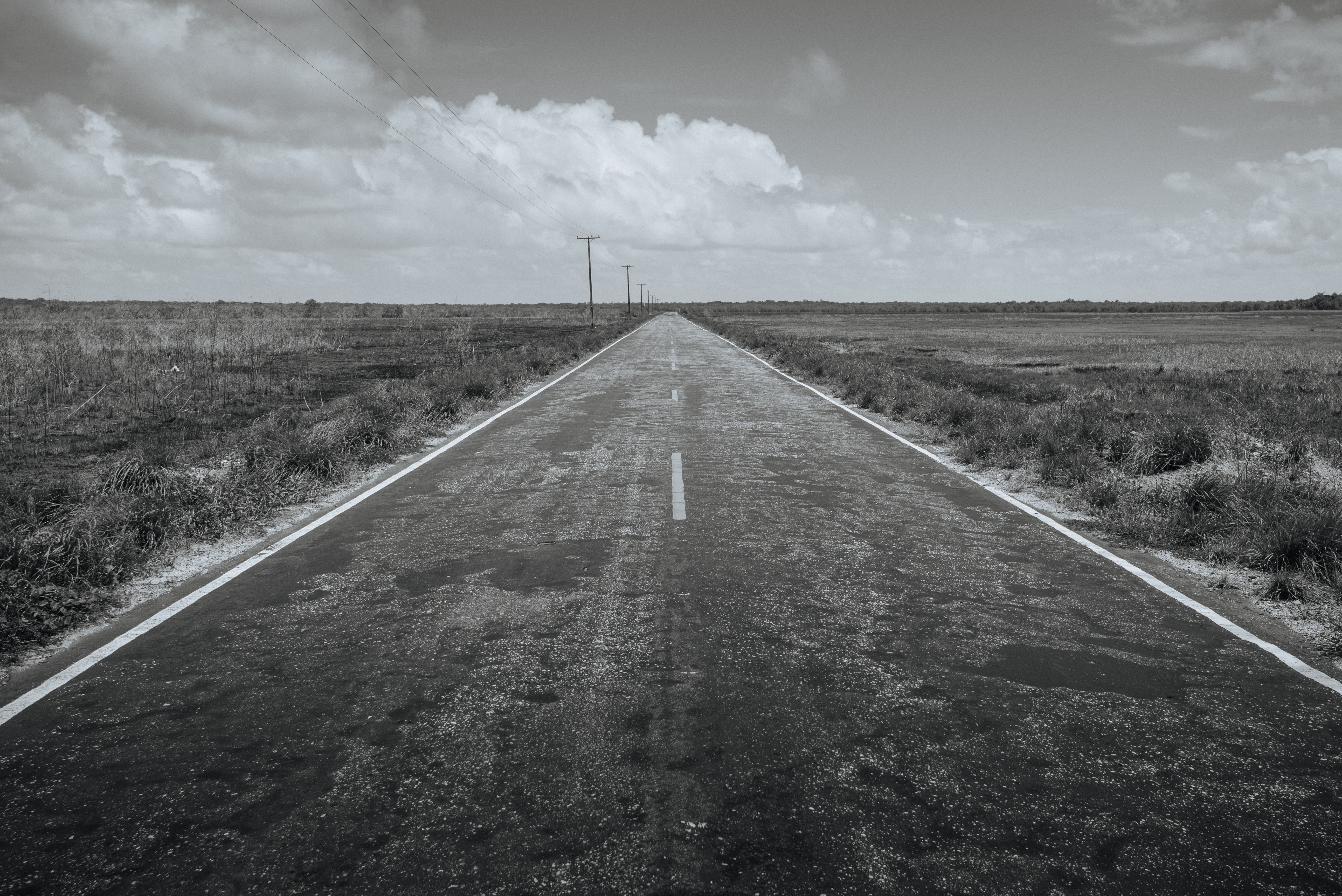 Black and white image of a long, empty road stretching to the horizon. HD Wallpaper