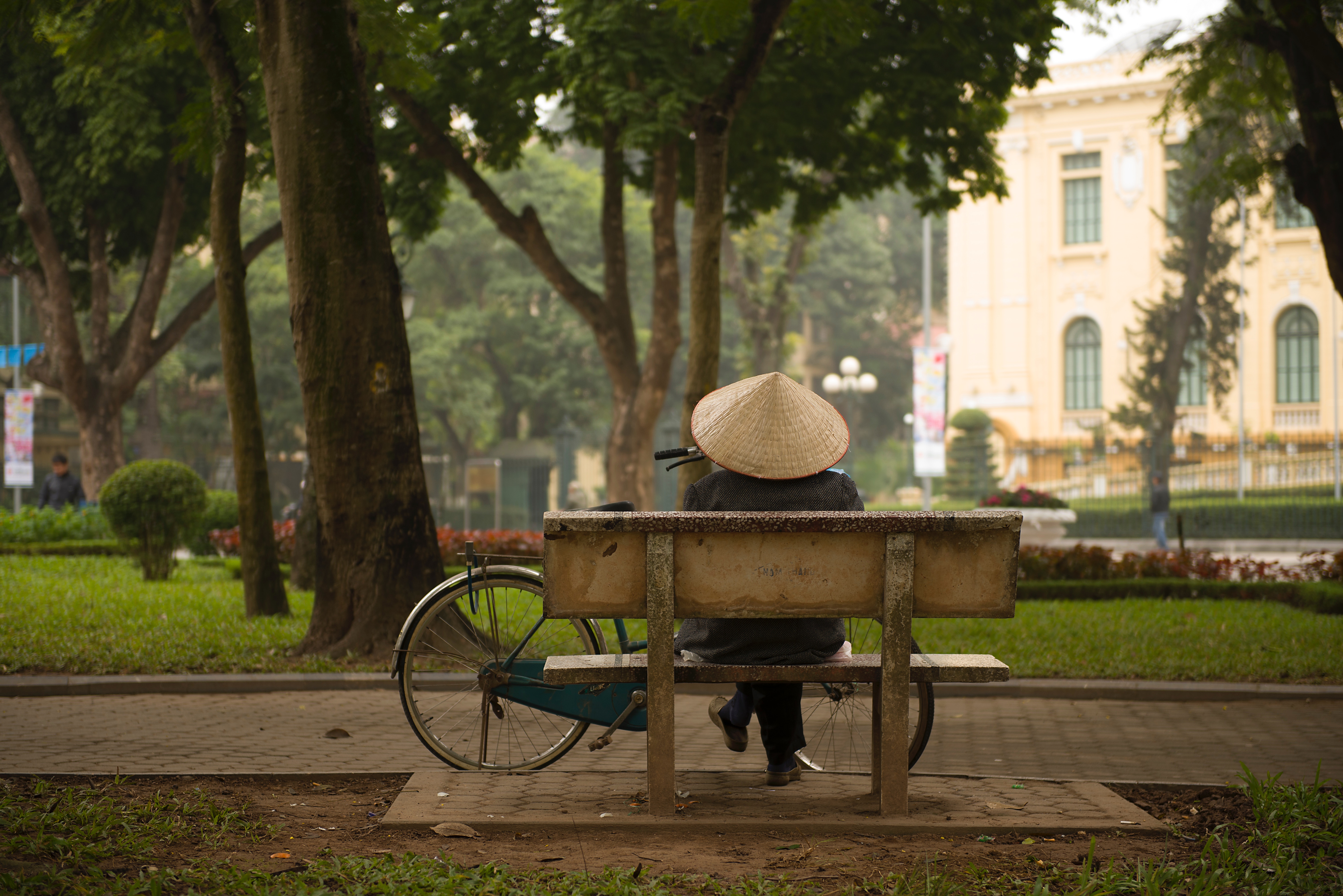 Person in conical hat on park bench with bicycle HD Wallpaper
